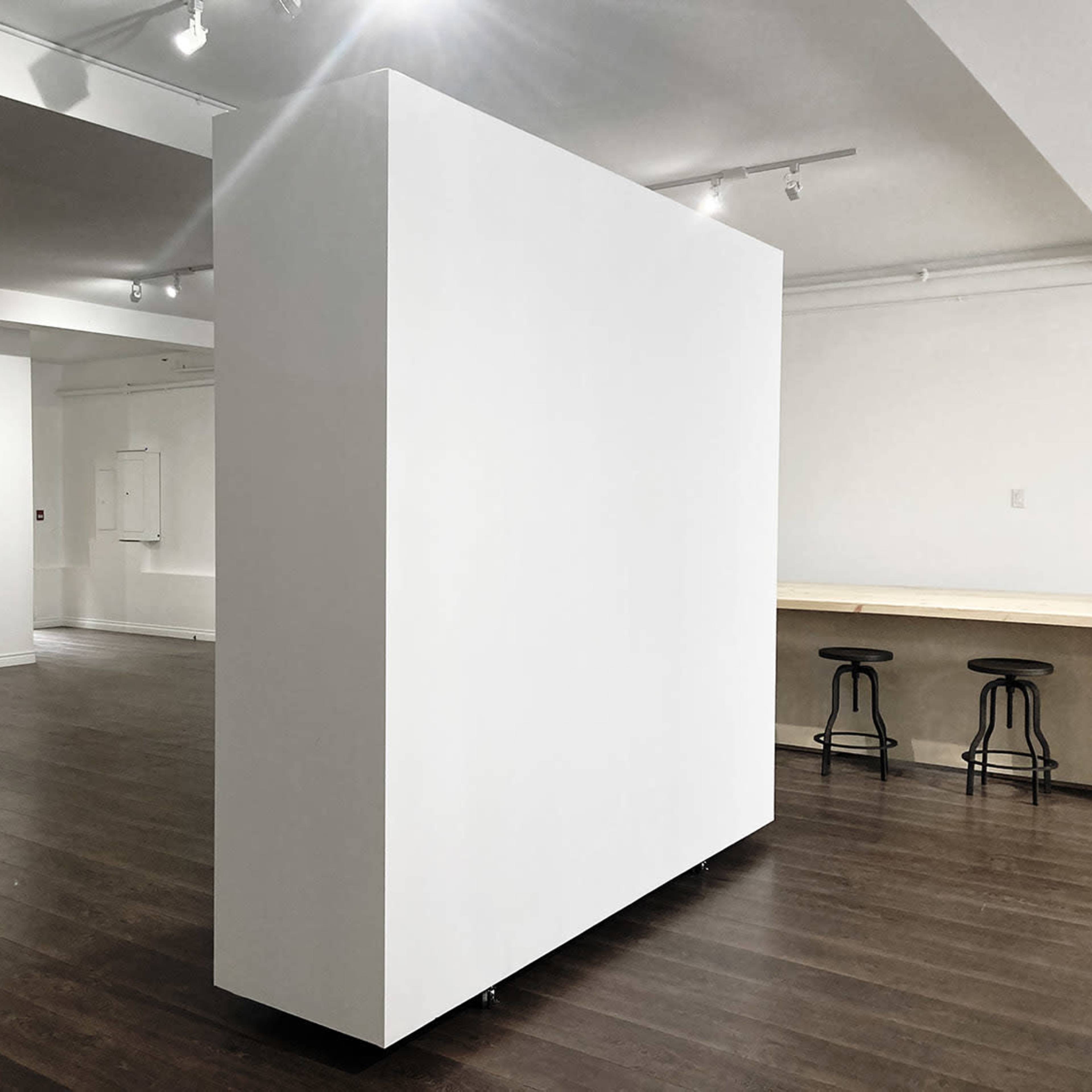 A spacious, minimalist room featuring a large white partition and wooden seating along one wall.