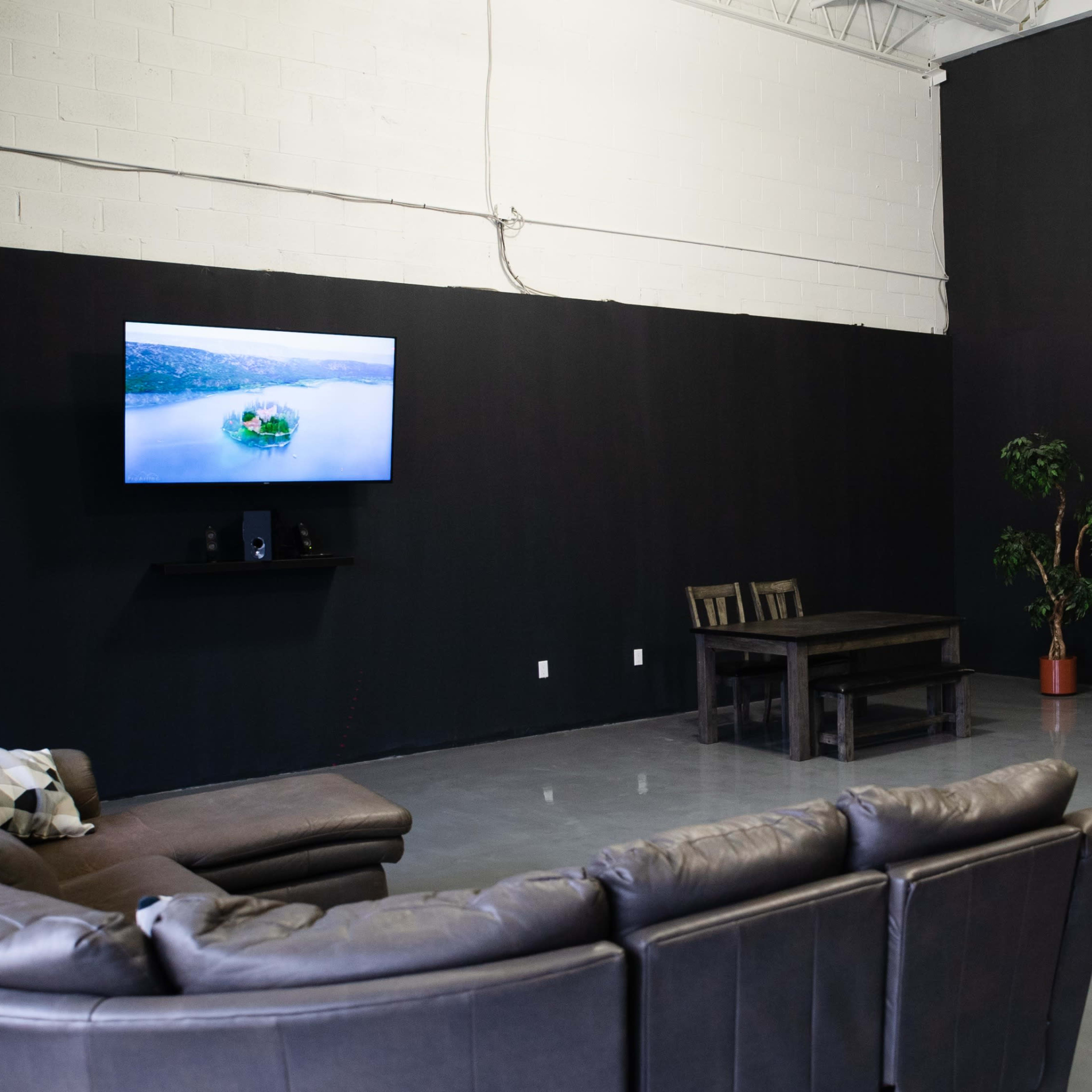 A spacious room with a dark wall, featuring a large TV mounted on one side, a sleek reception desk, a coffee table, and a sofa arranged for seating.