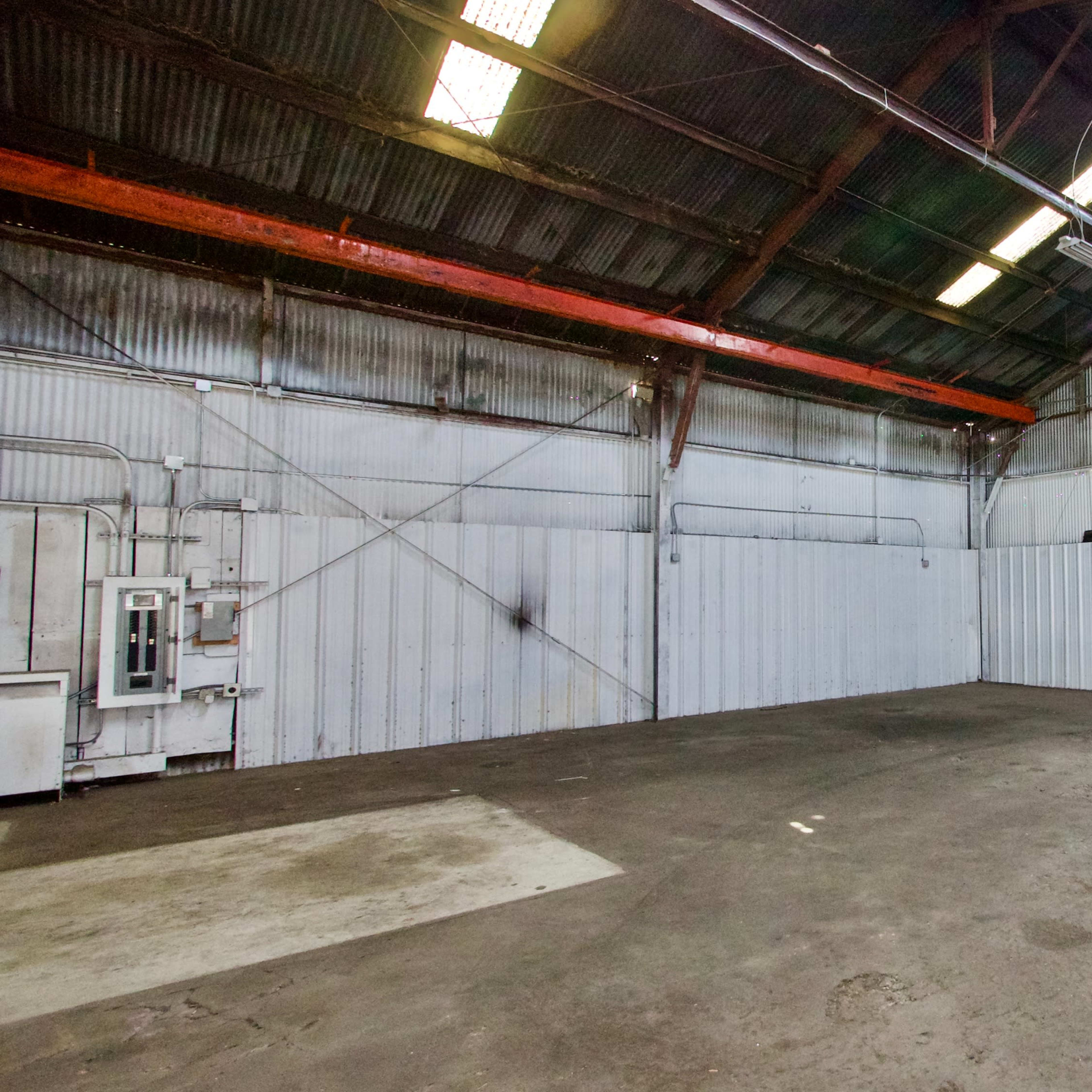 An empty industrial warehouse interior with metal walls, a concrete floor, and large overhead beams.