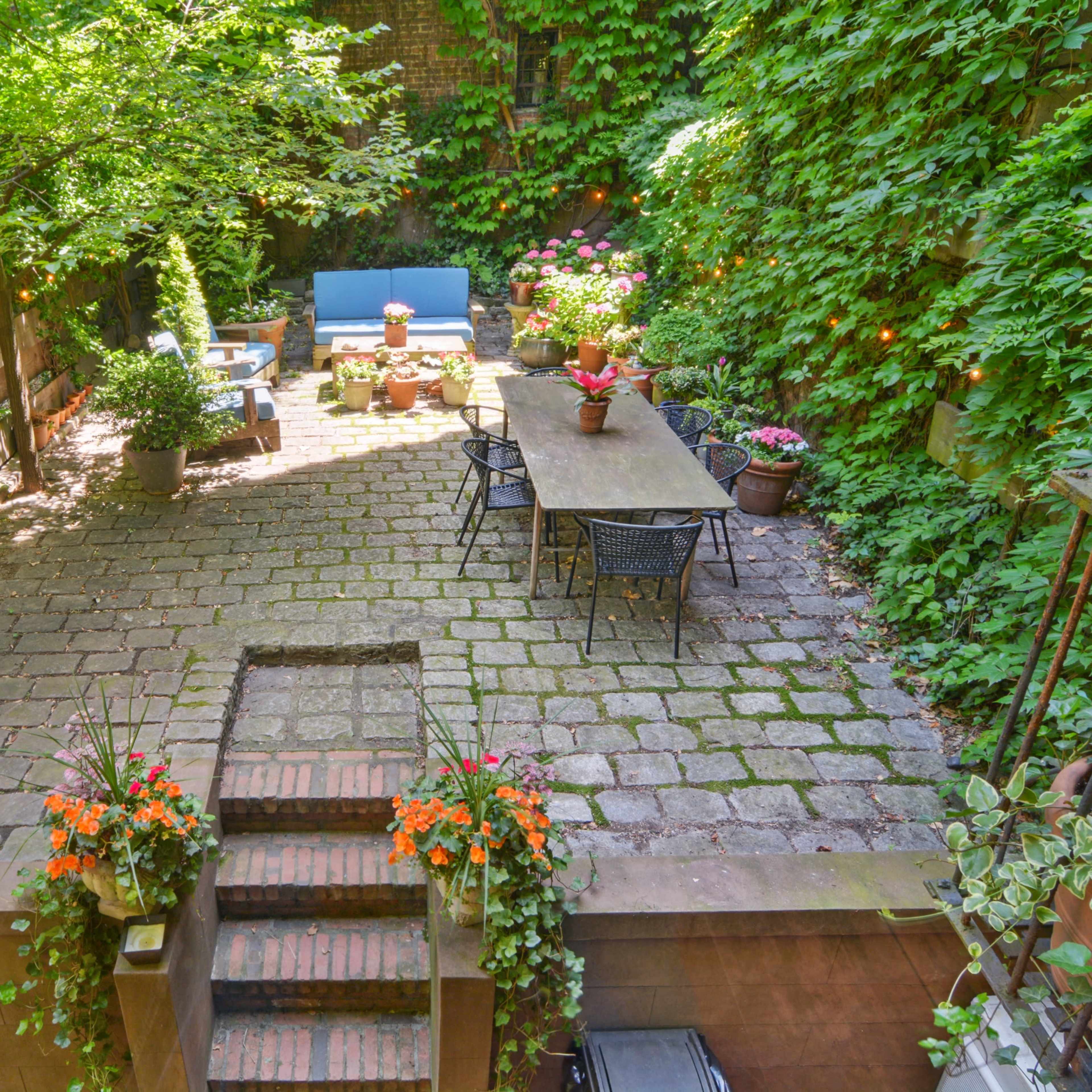 A stone-paved courtyard surrounded by lush greenery, featuring seating areas with potted plants.