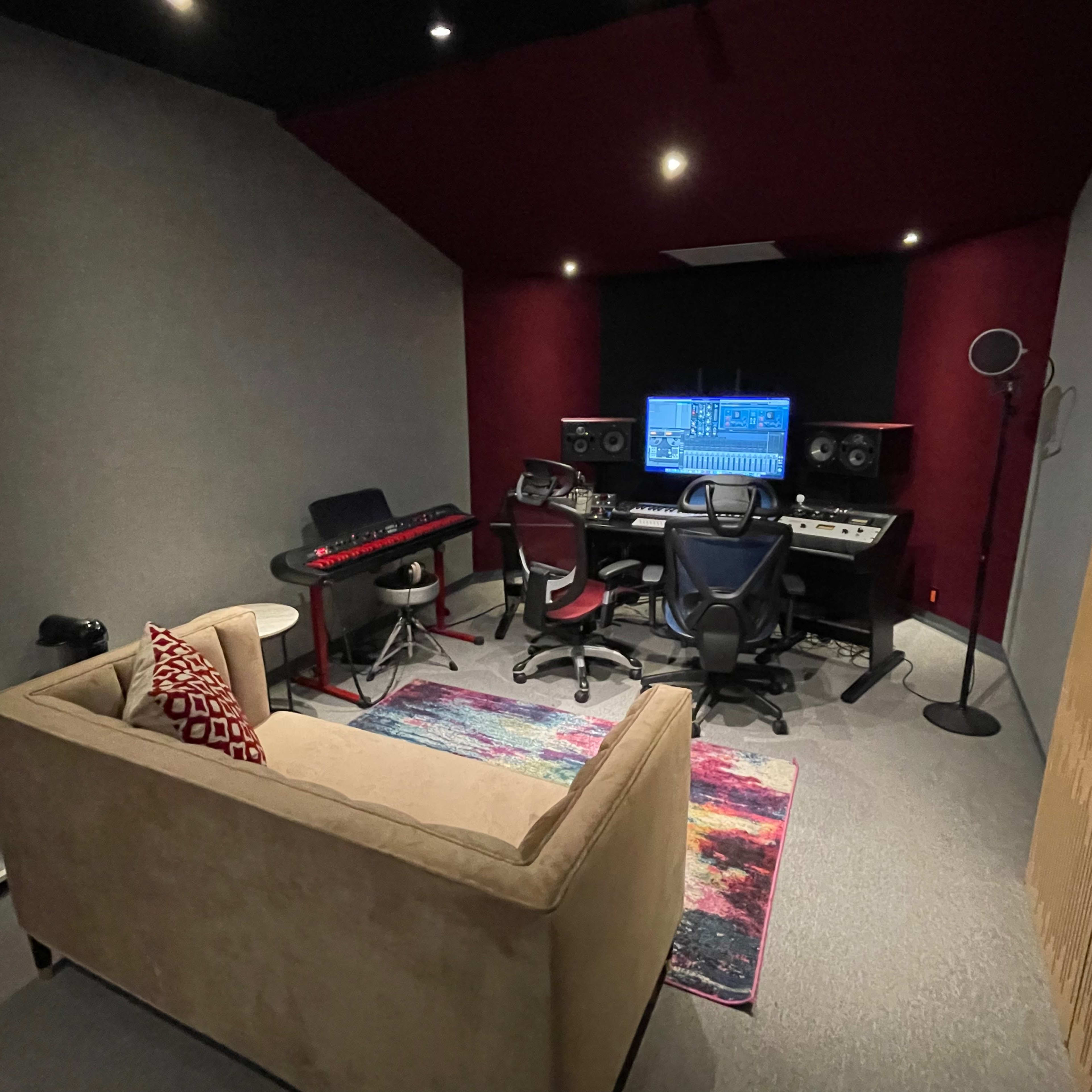 A music studio with a mixing desk, musical instruments, a chair, and a couch in a room designed for sound production.