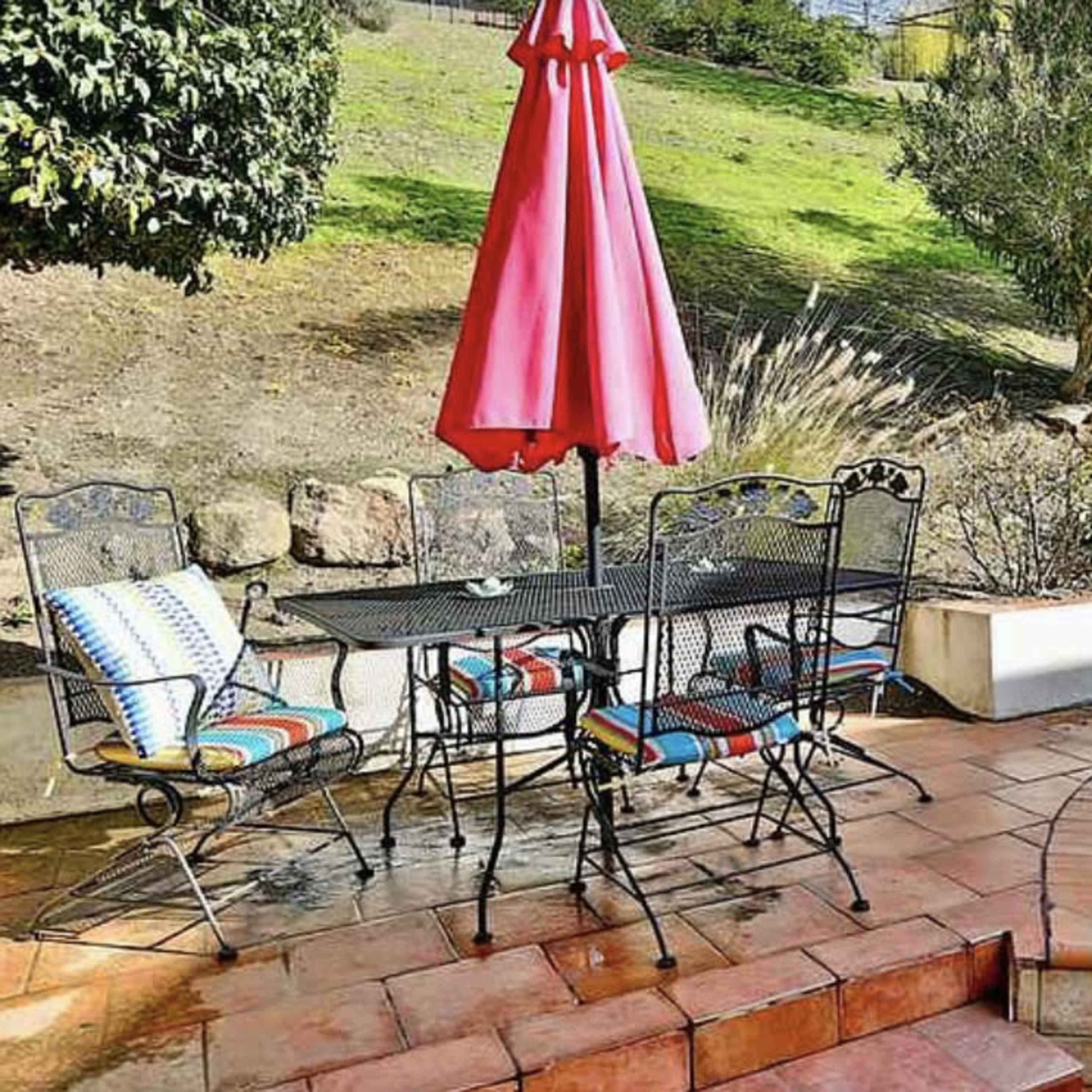 A patio area features a round table with four chairs and a large pink umbrella beside a swimming pool.