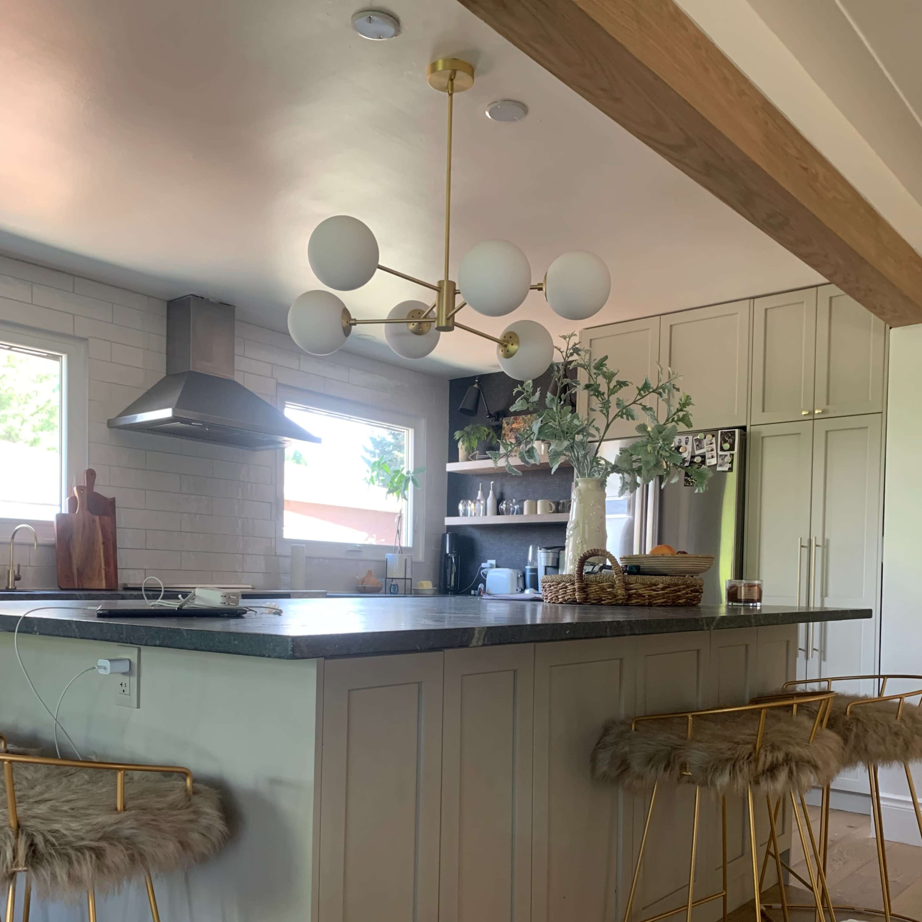 A modern kitchen with a central island, featuring bar stools, a pendant light, and organized shelves with kitchenware.