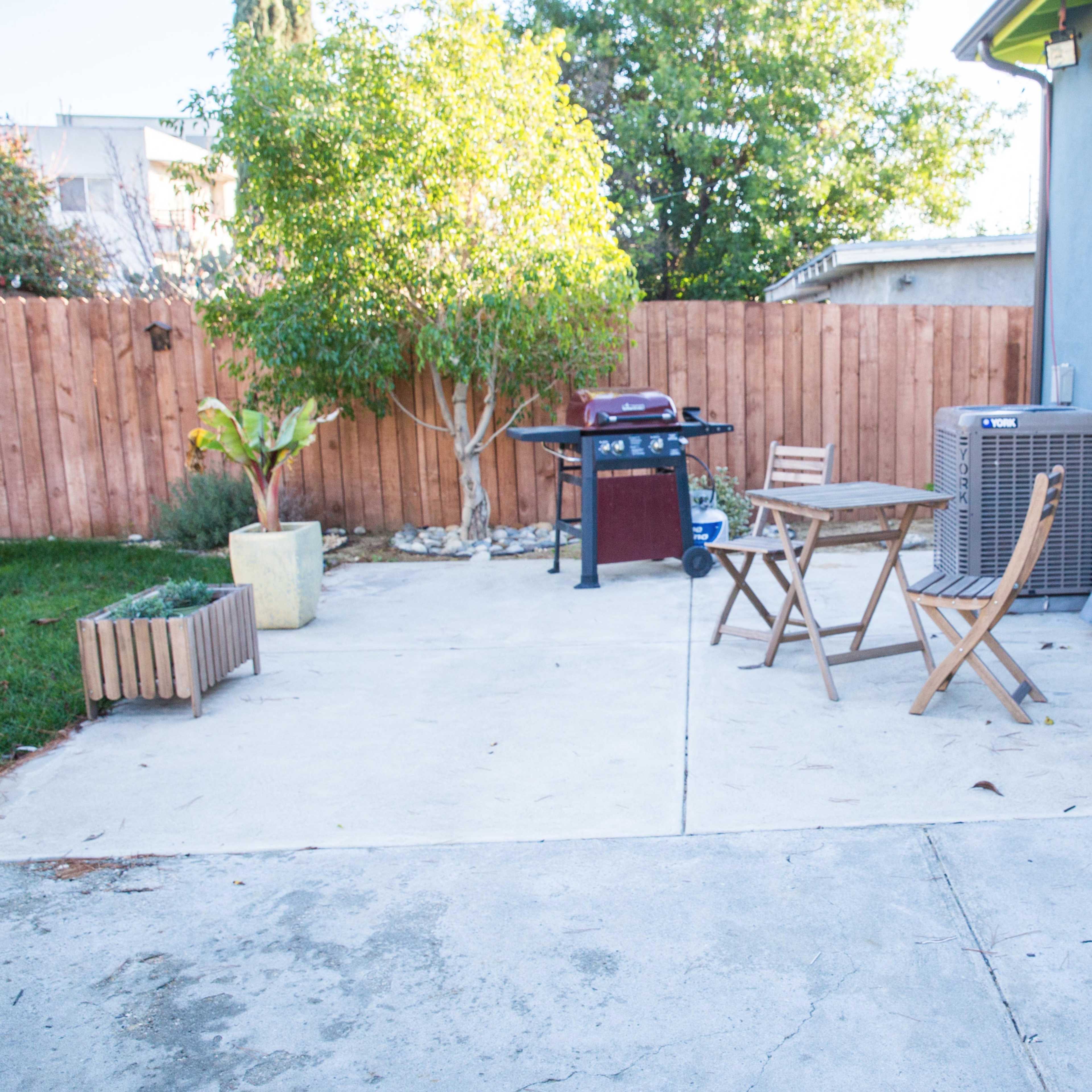 A patio area with a grill, a small table and chairs, and decorative letters spelling "LOVE" against a blue wall.