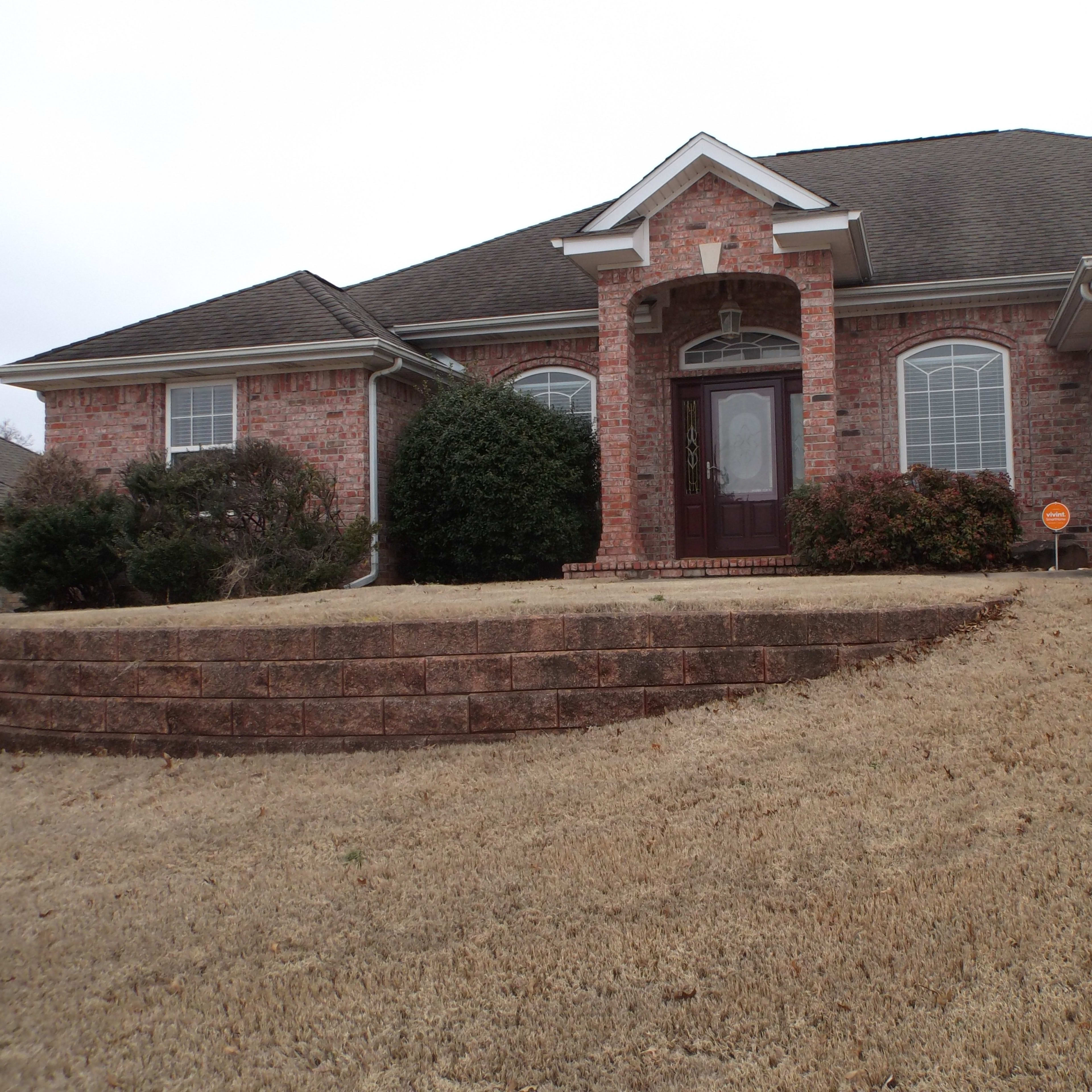 A single-story brick house with a front porch and landscaped yard sits on a gently sloping lot.