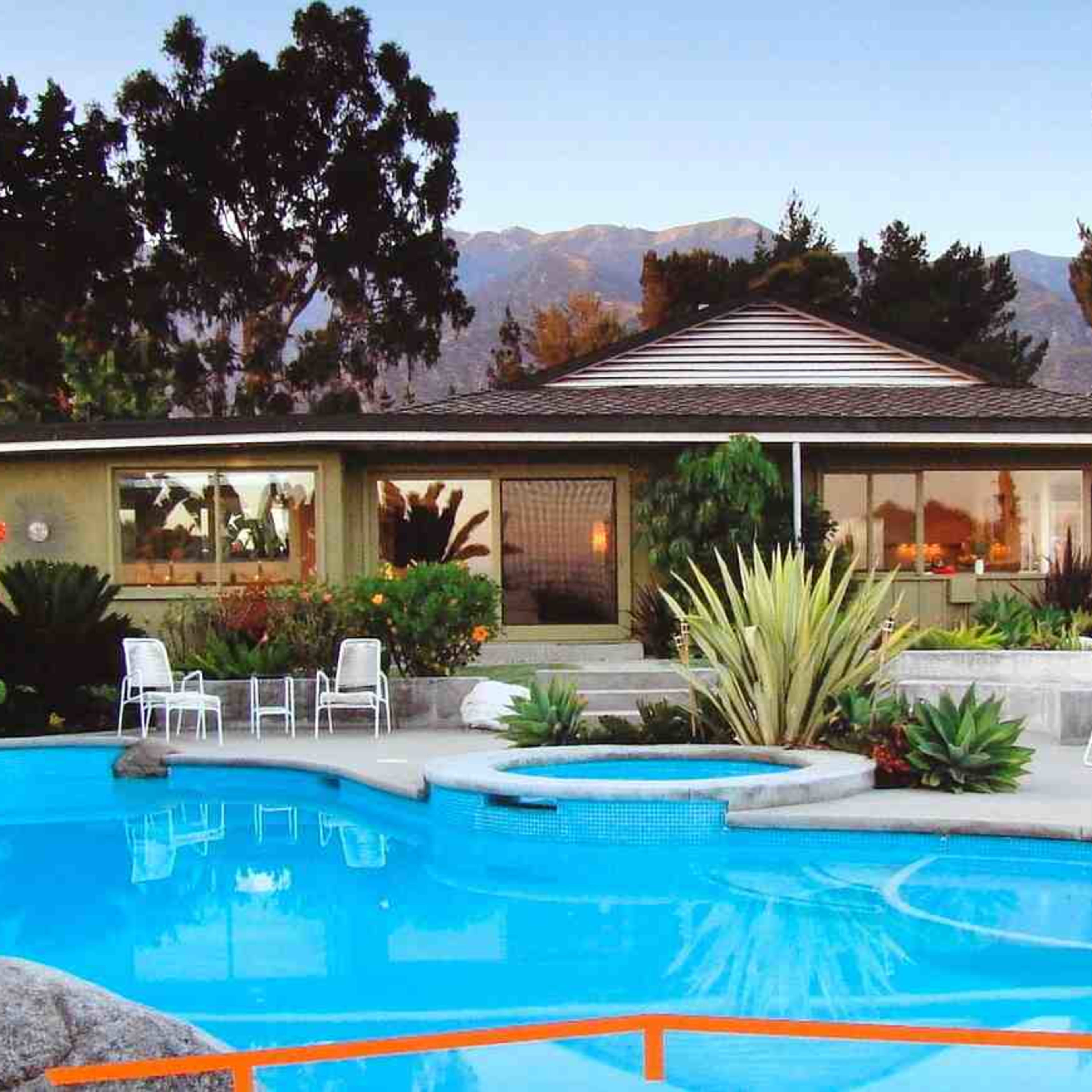 A modern house with large windows, surrounded by a landscaped garden and a swimming pool with lounge chairs.