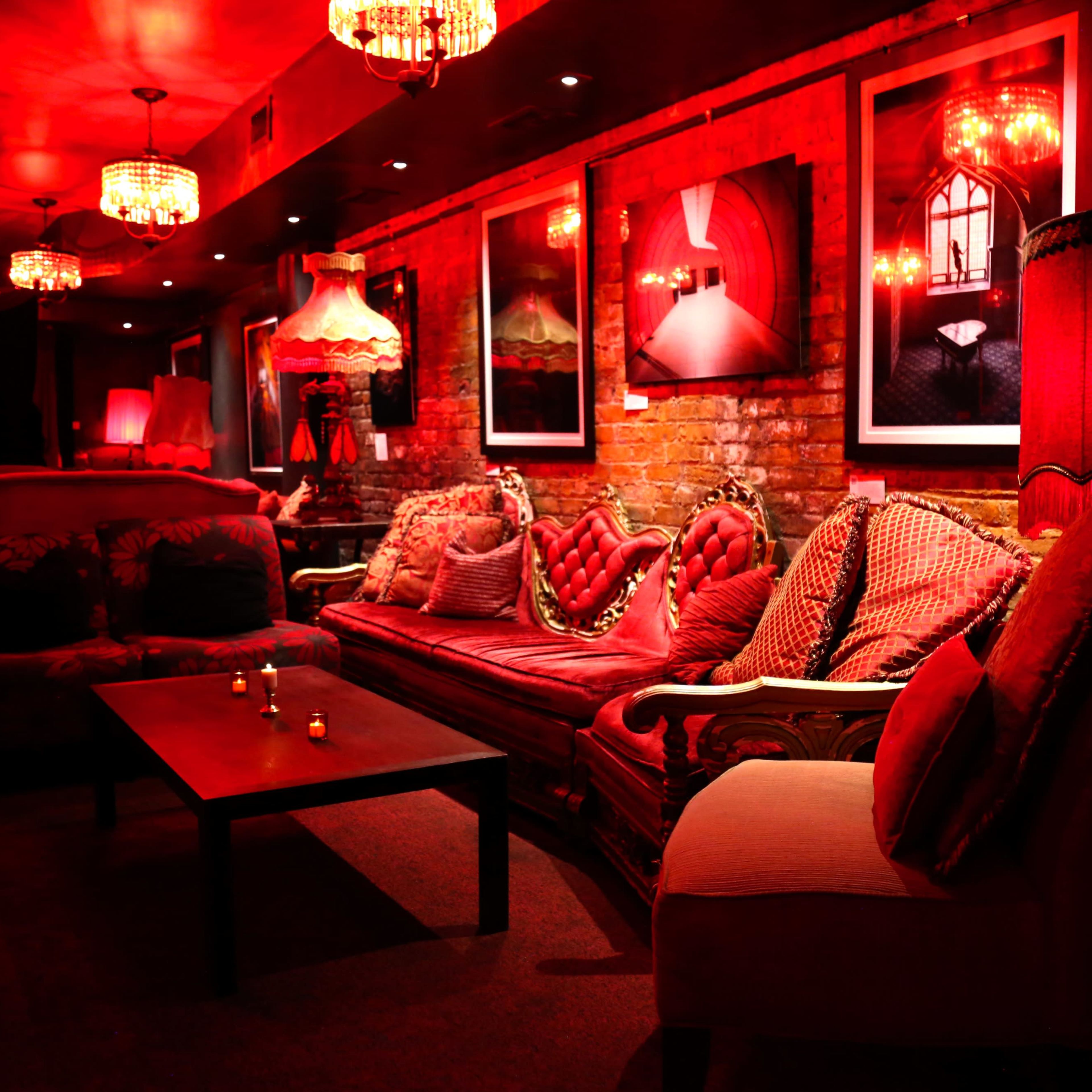 The scene shows a dimly lit lounge with red lighting, featuring plush seating and decorative artwork on the walls.