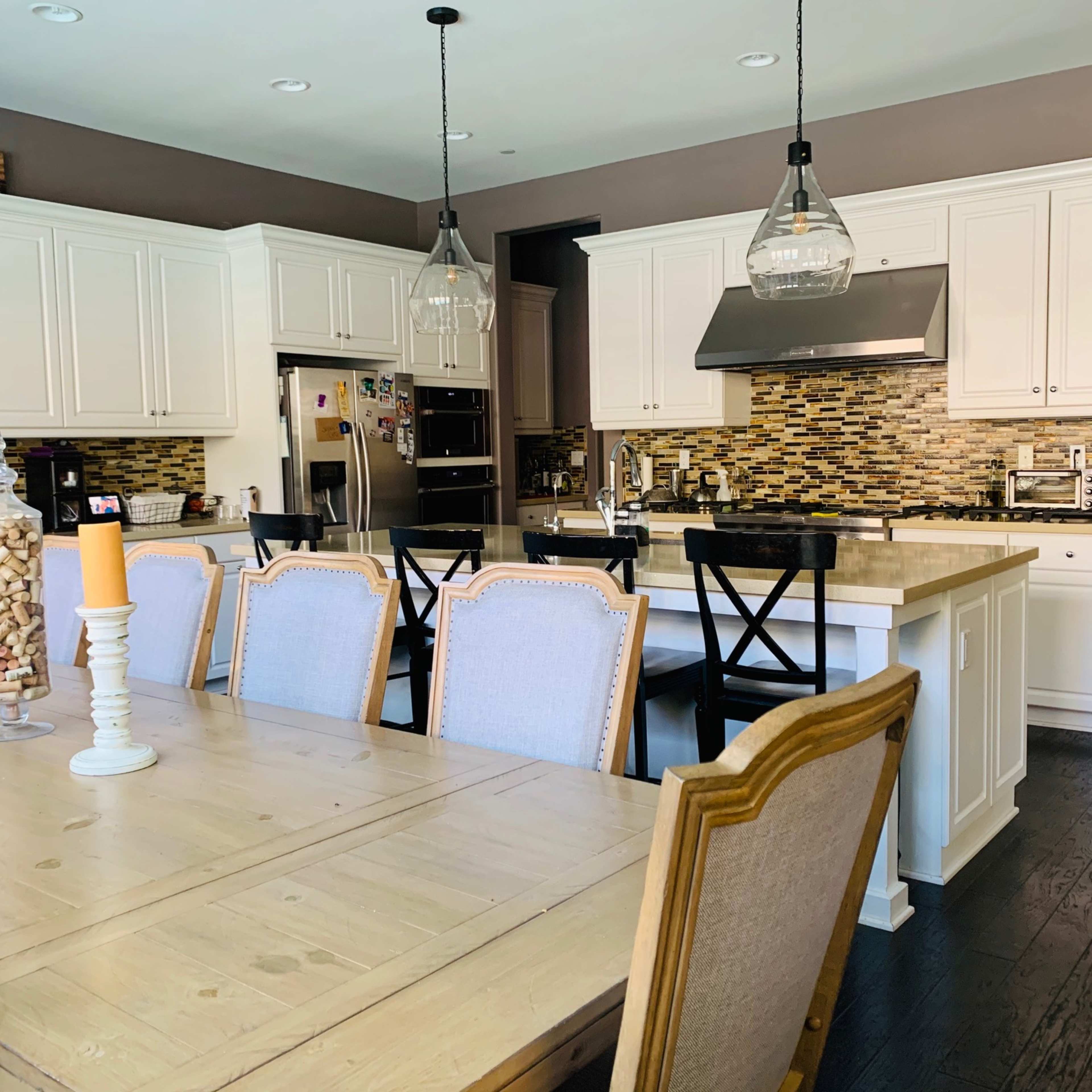 A modern kitchen features white cabinetry, a central island, and a large dining table with six chairs.