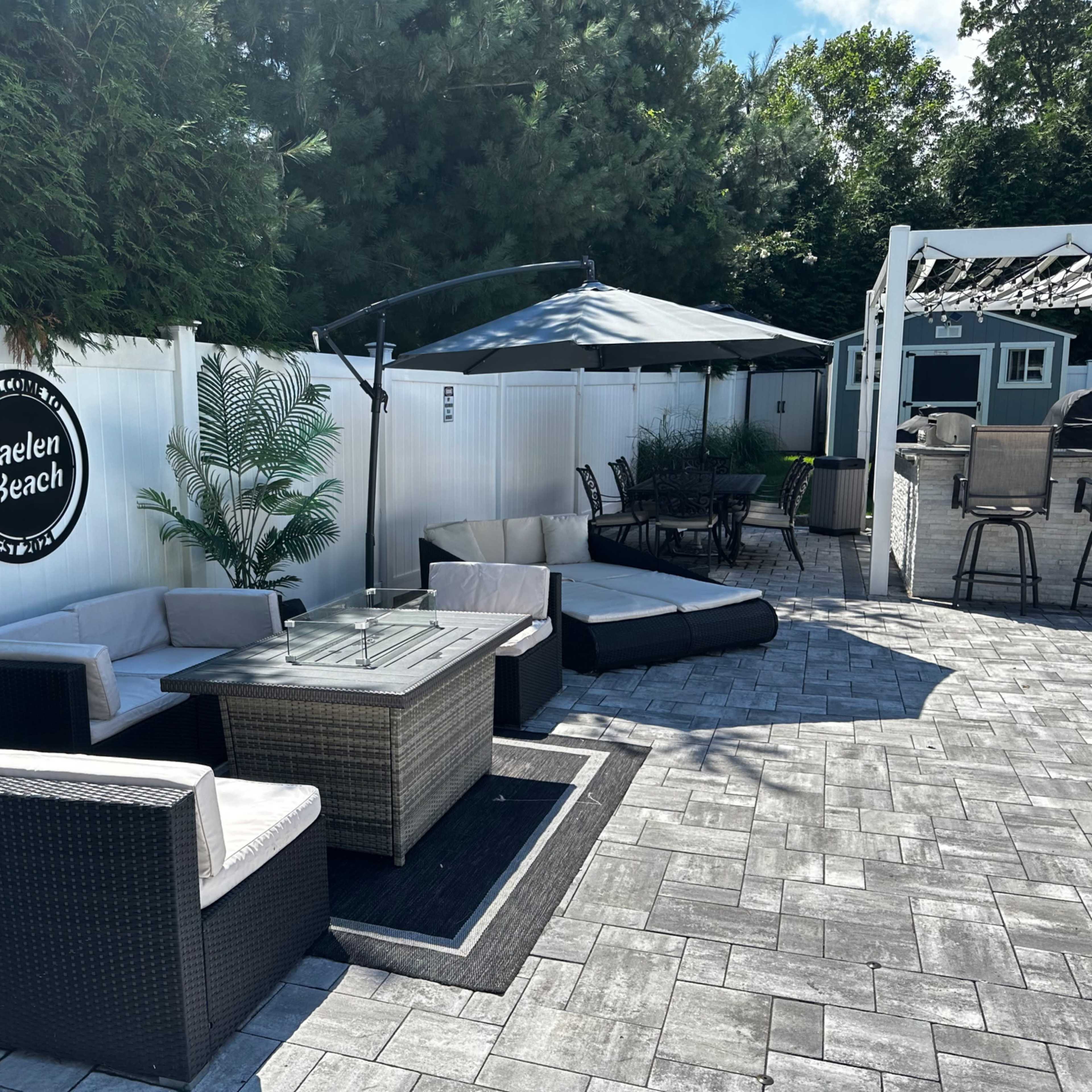 A neatly arranged outdoor lounge area with a coffee table, seating, and a canopy in a well-maintained garden setting.