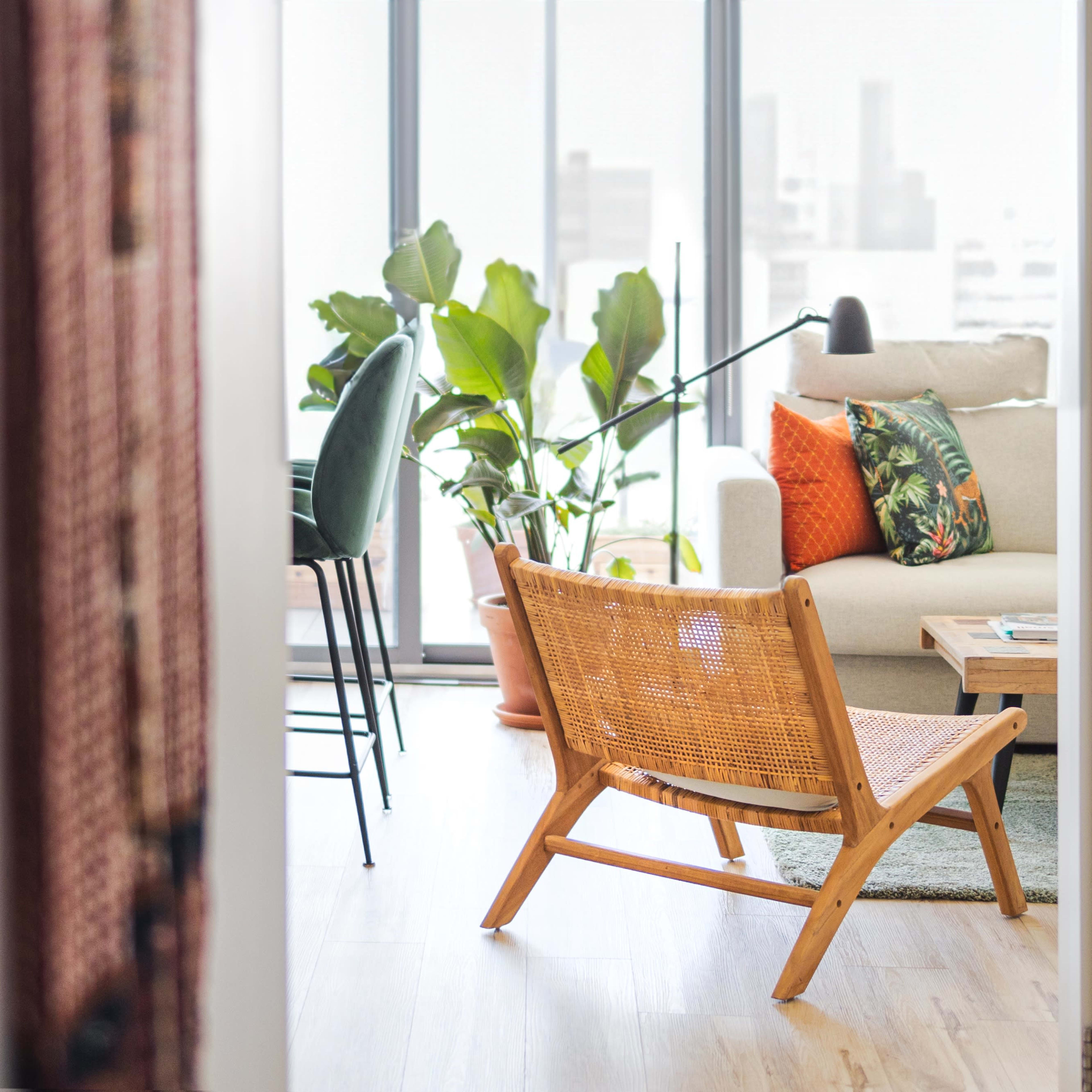A wooden chair faces a living room with a sofa, a coffee table, and large windows overlooking city buildings.