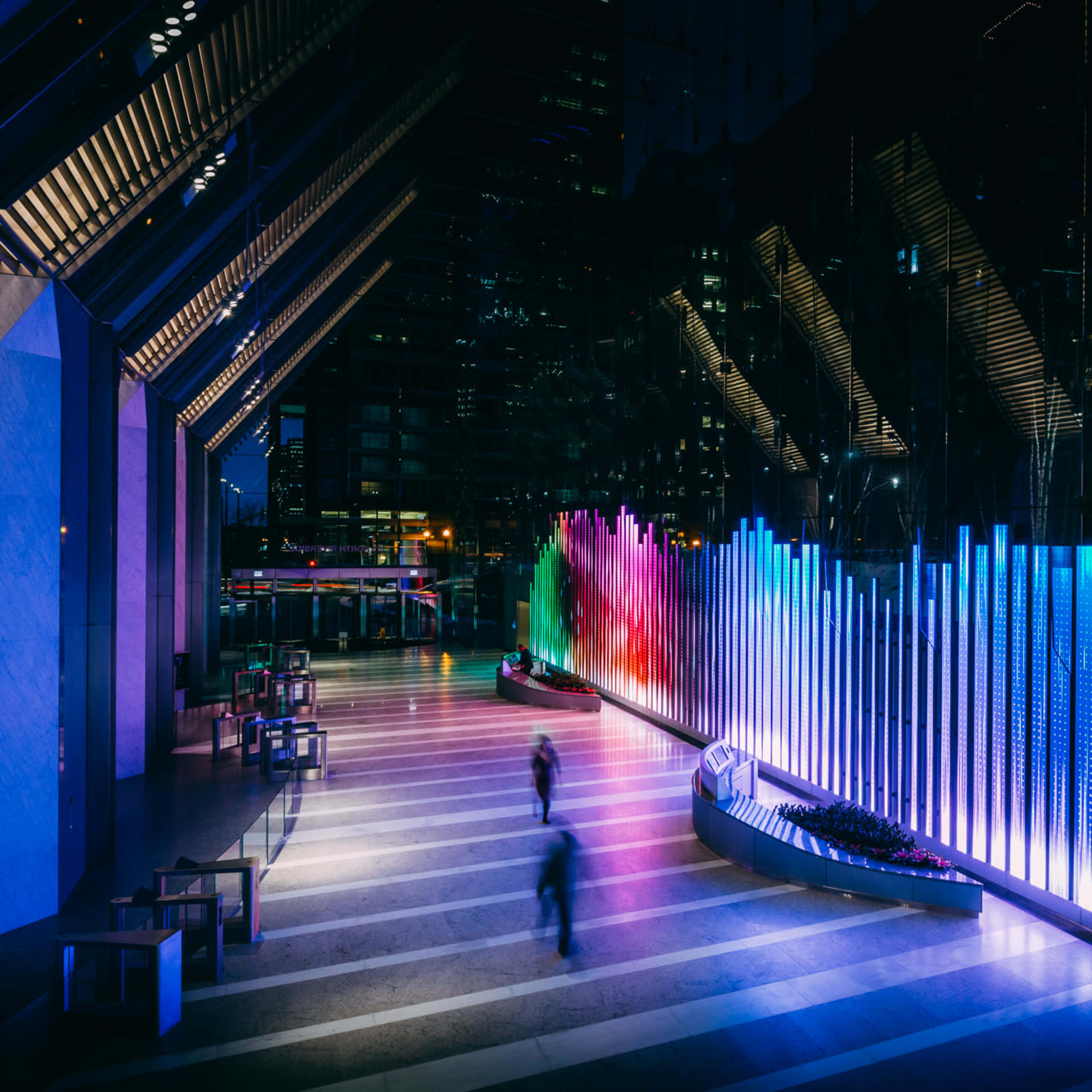 The scene features a modern indoor space with illuminated vertical lights creating a colorful display along one wall, while figures move through the area.
