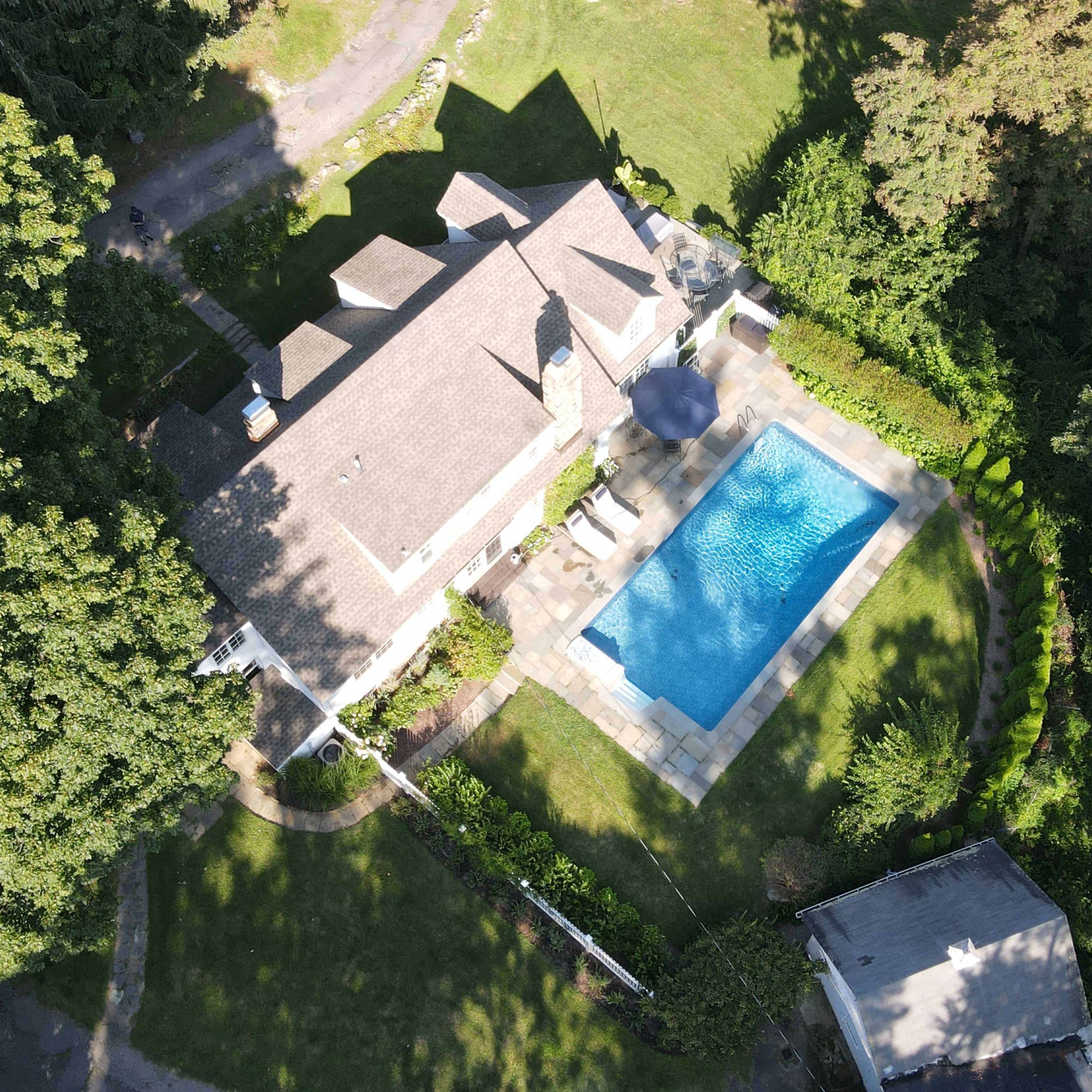 A residential property with a swimming pool surrounded by greenery, viewed from an aerial perspective.