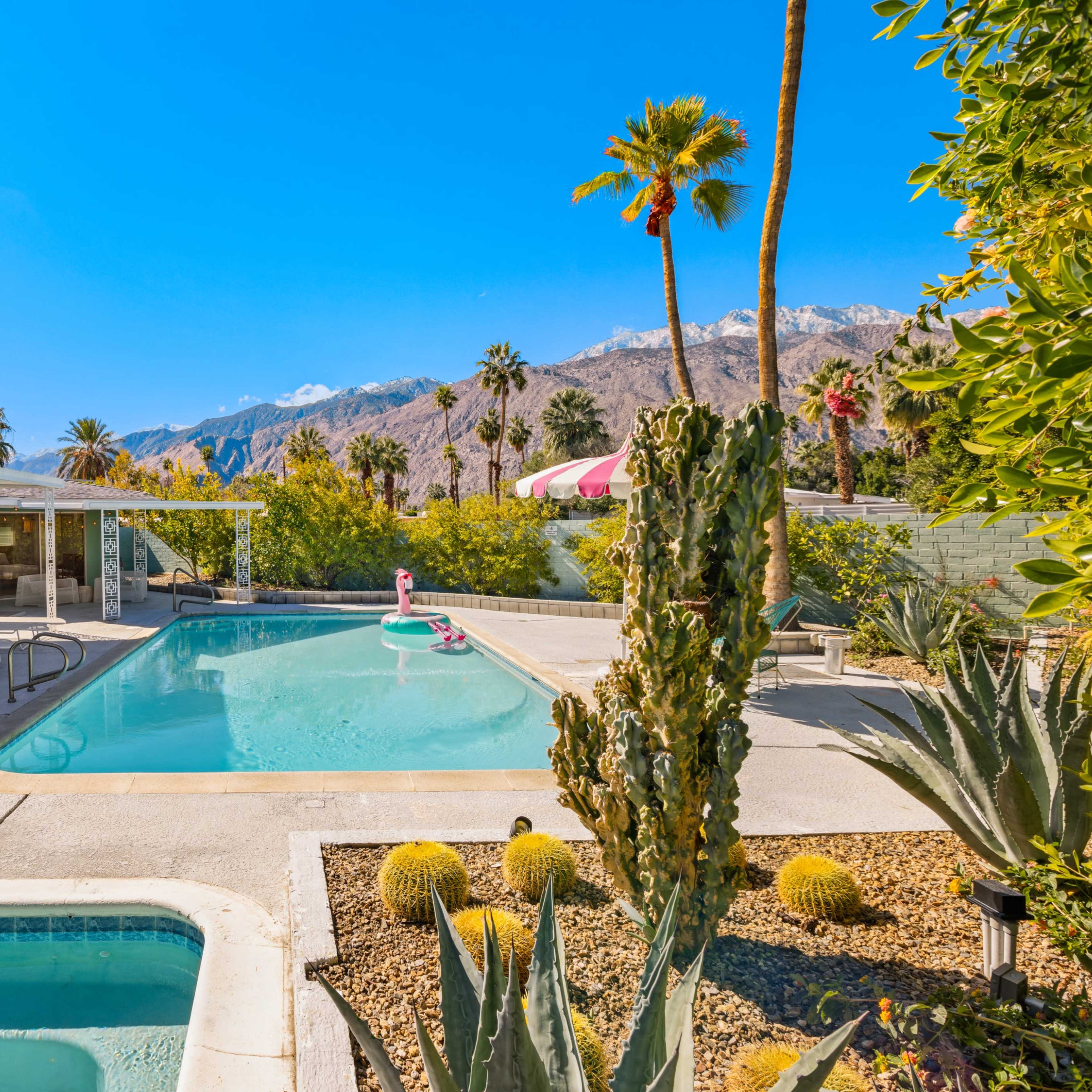 A swimming pool surrounded by palm trees and desert landscaping with mountains in the background.