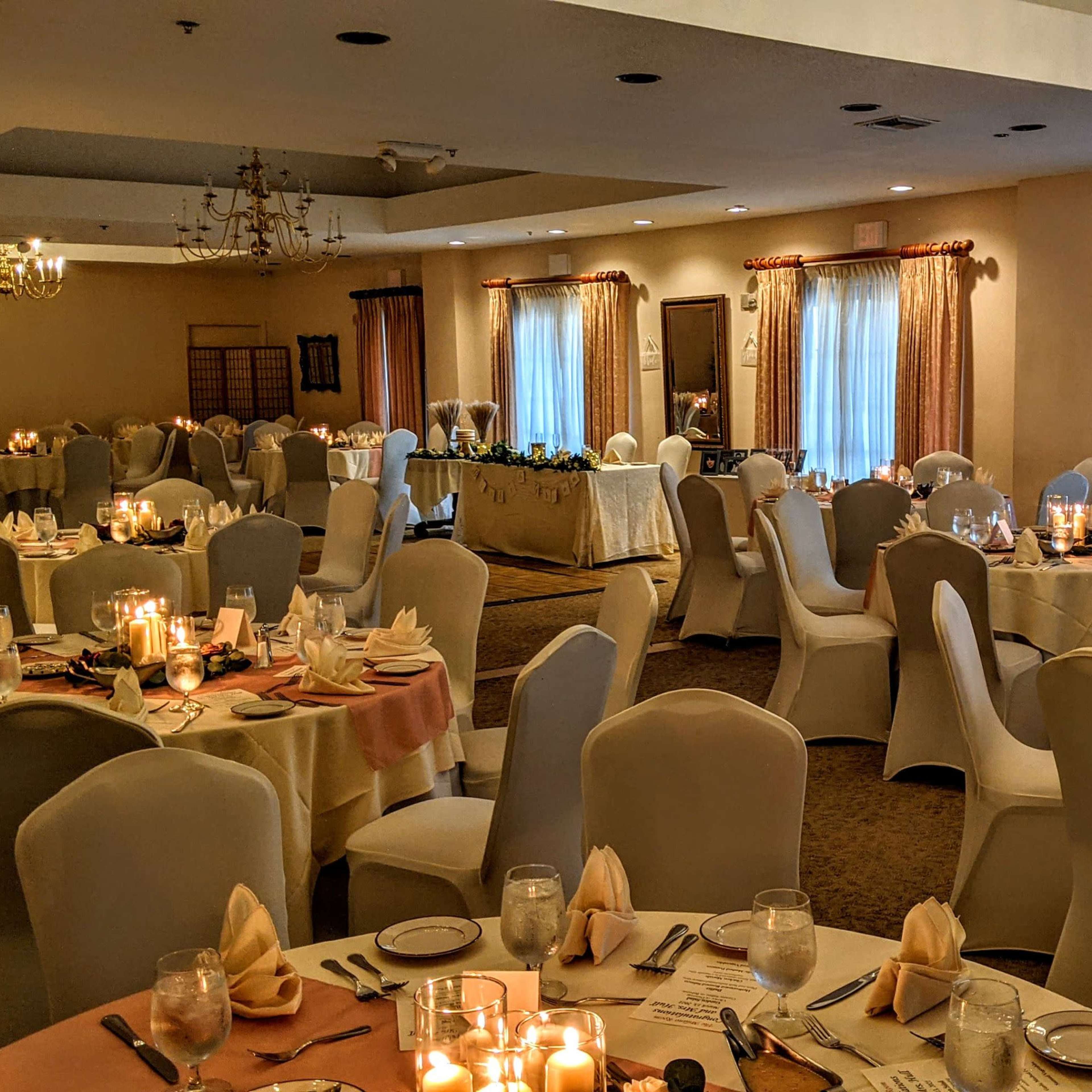 A banquet hall set up for an event, featuring neatly arranged tables with white tablecloths, candles, and place settings.