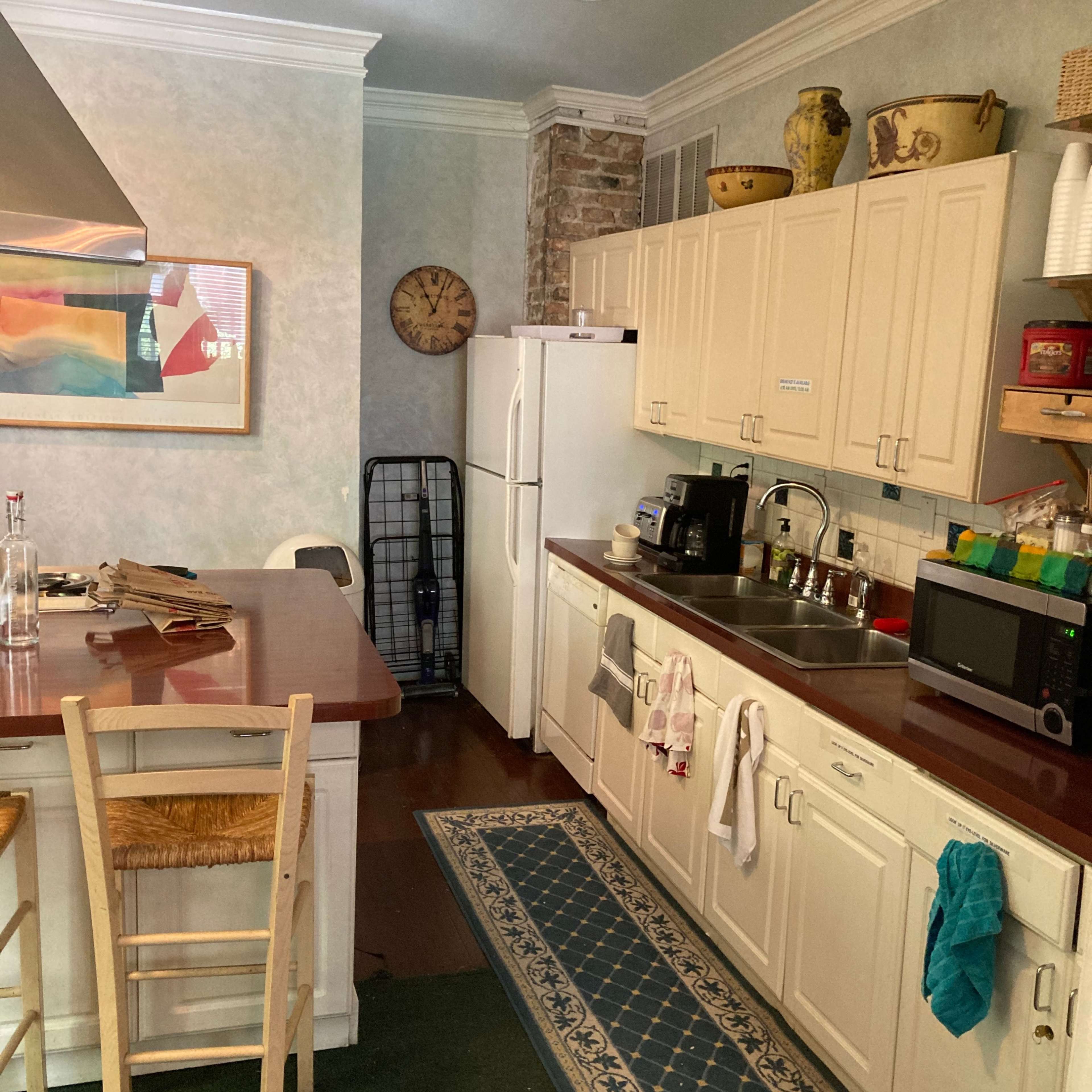 The kitchen features a wooden island with a countertop, a refrigerator, a sink with cabinets underneath, and various appliances along the walls.
