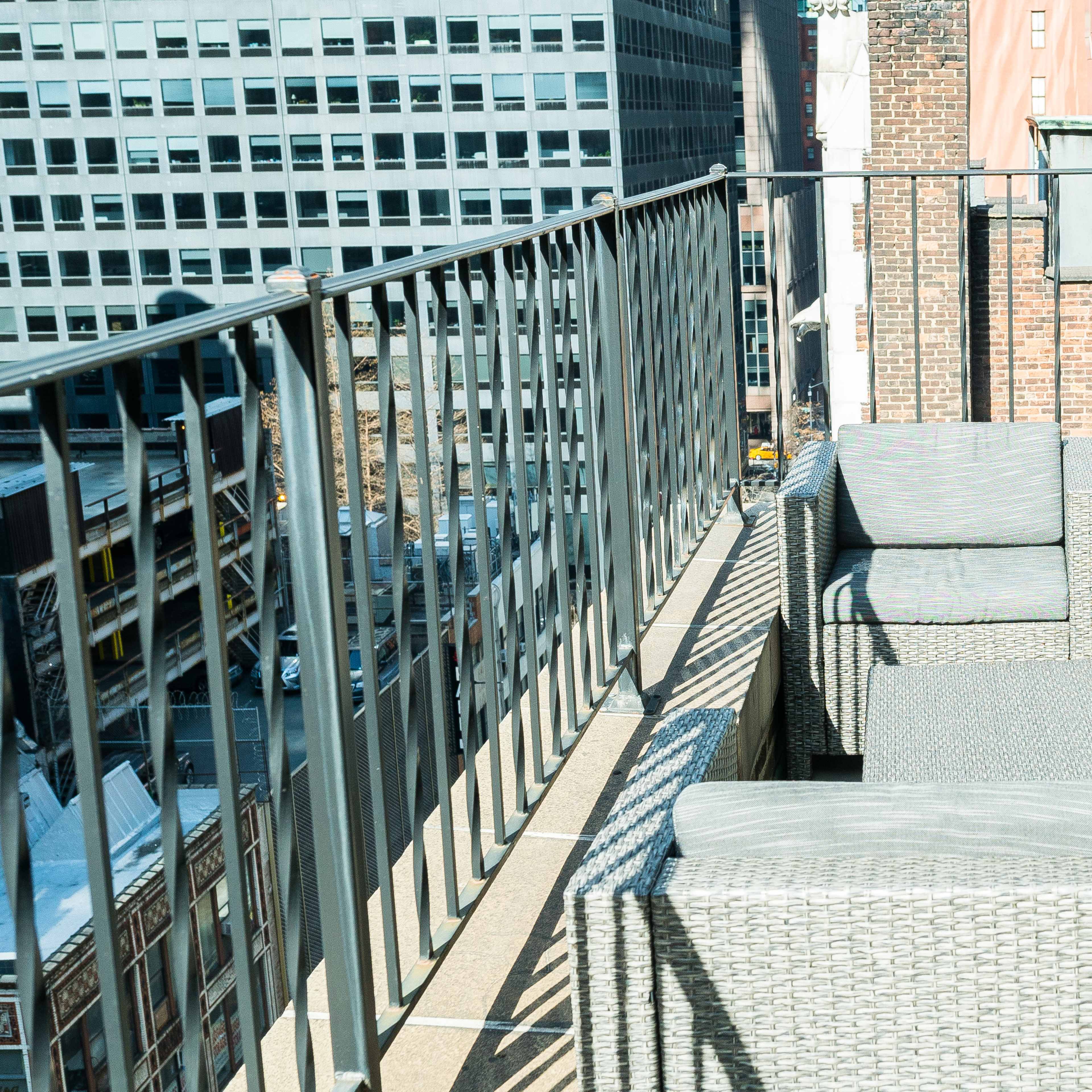 A rooftop terrace with wicker furniture and a potted plant overlooking a city skyline.