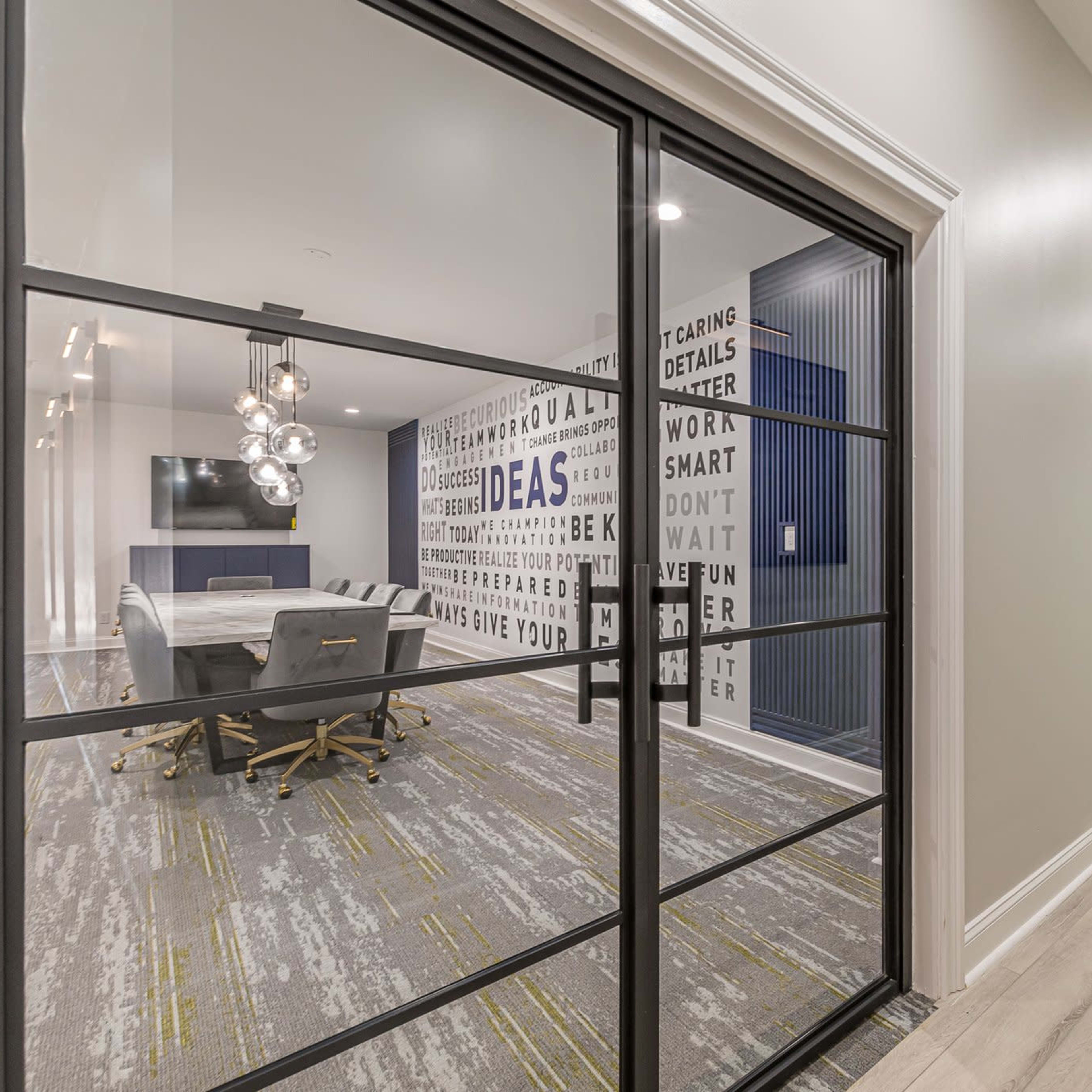 A modern office space with a glass partition, featuring a conference table and walls decorated with motivational words.