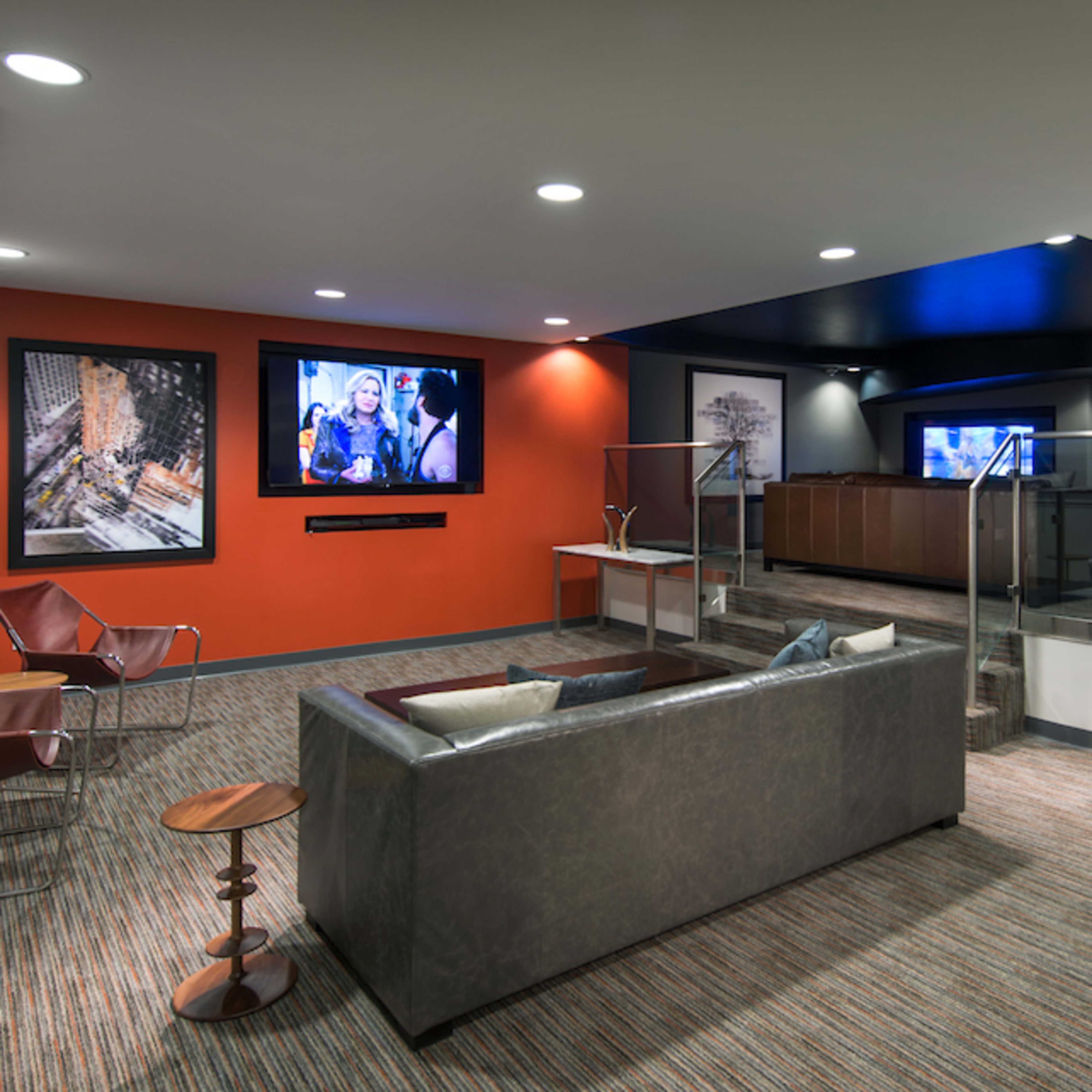 A modern lounge area with a sofa, armchairs, and a large screen displaying a video, set against a backdrop of contrasting colored walls and a reception area in the background.