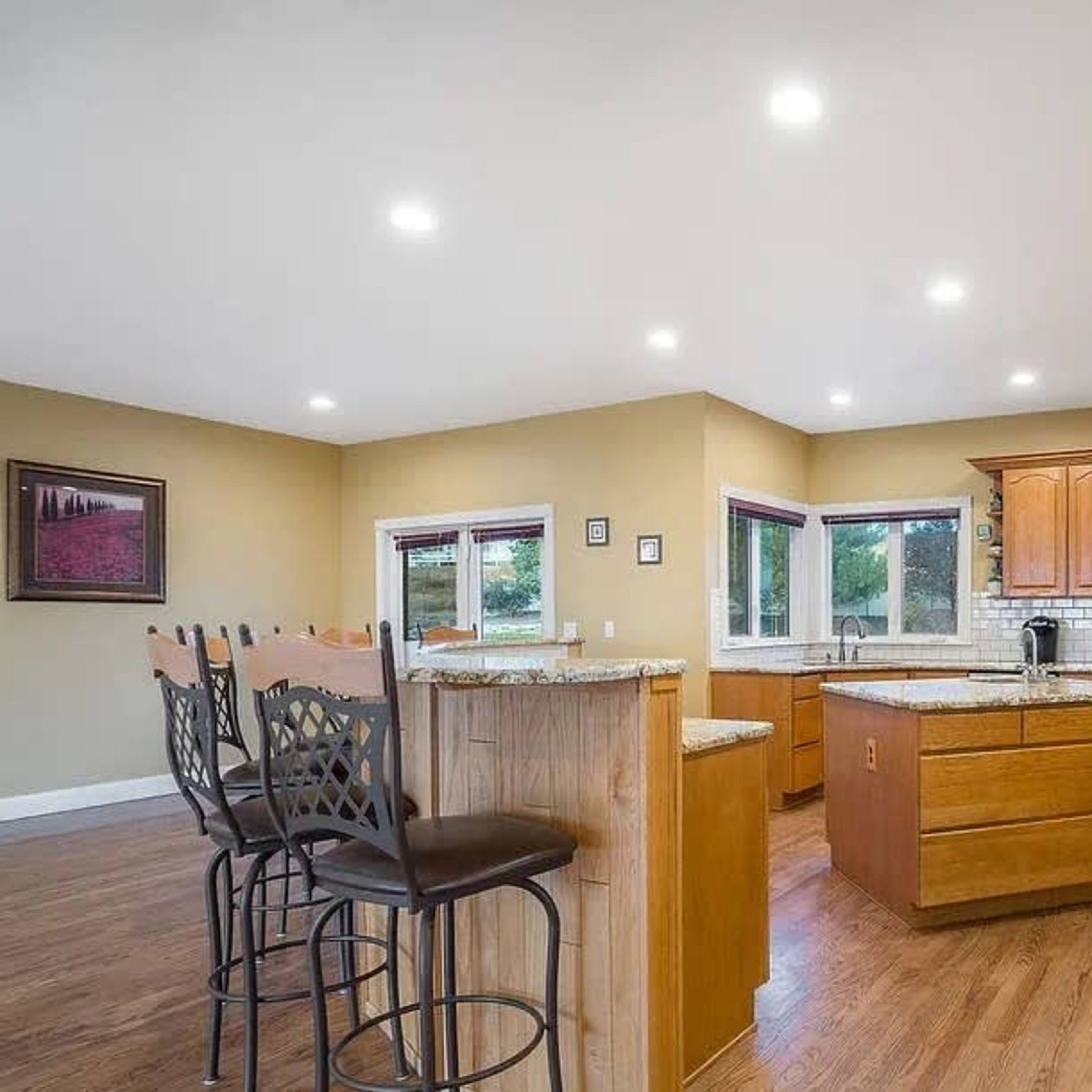 A spacious kitchen with wooden cabinets, a central island, and modern appliances, illuminated by recessed lighting.