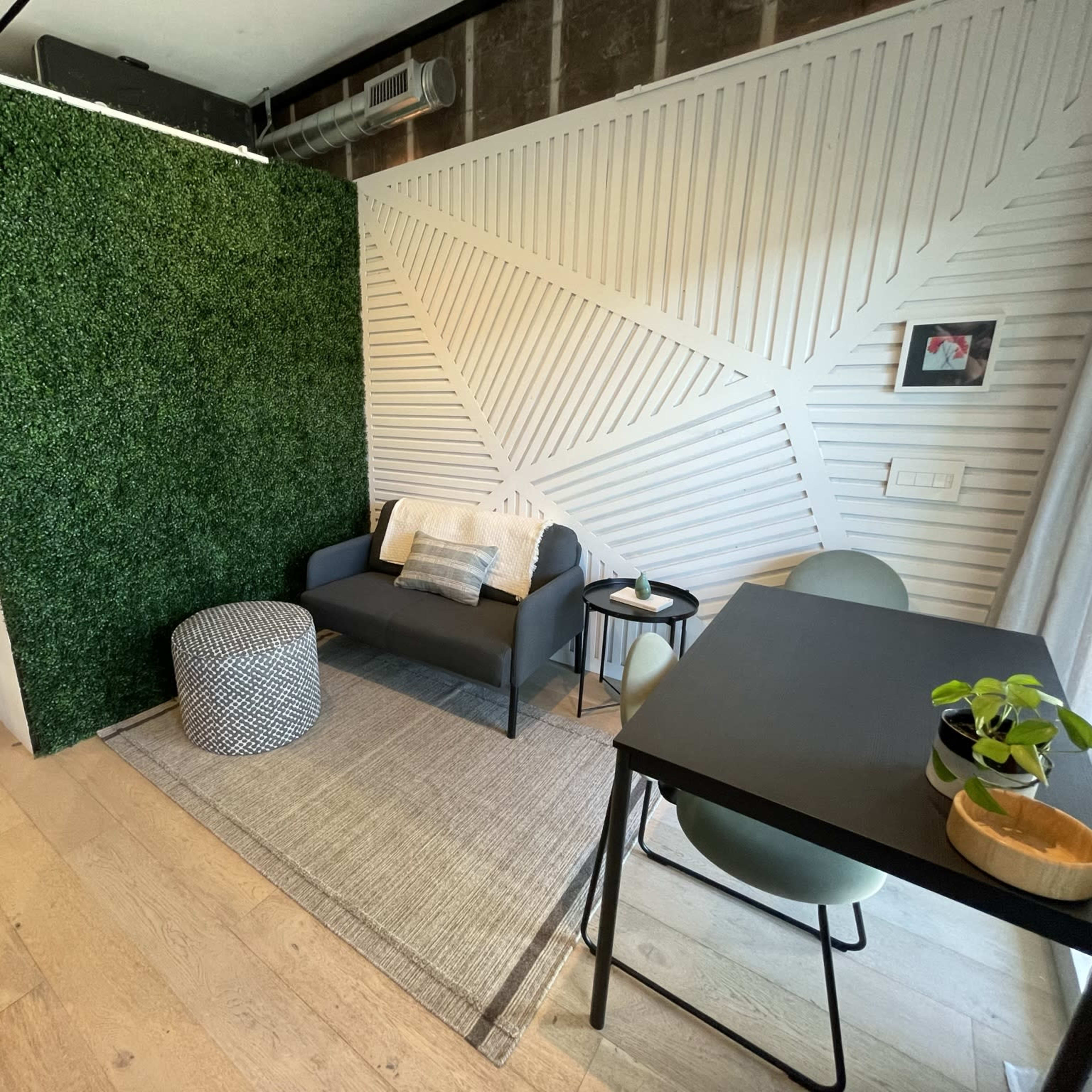 A modern interior room featuring a green wall, a small seating area with a couch and a round ottoman, and a dining table with chairs.