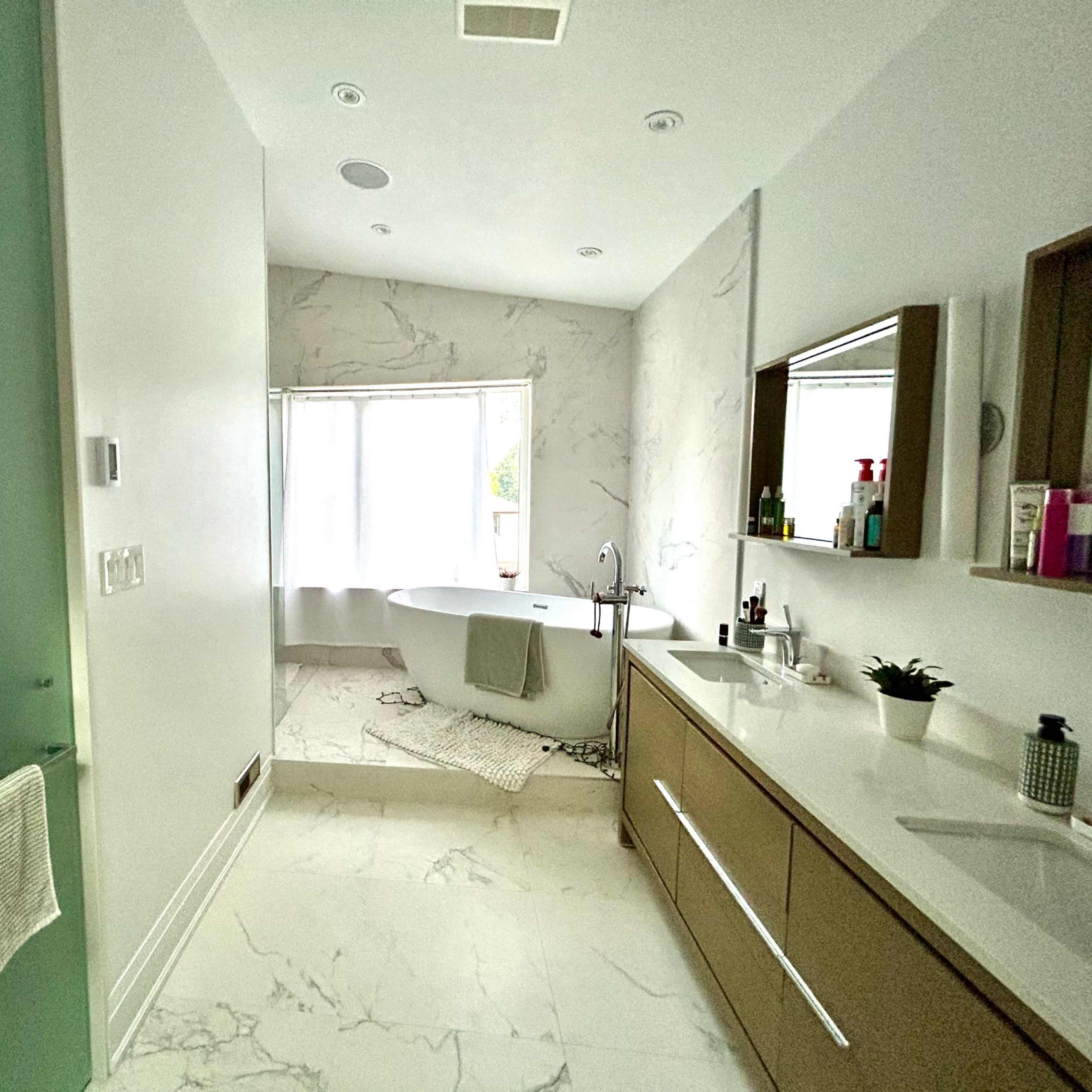 A modern bathroom features a freestanding bathtub, a double sink vanity, and a large window with natural light.