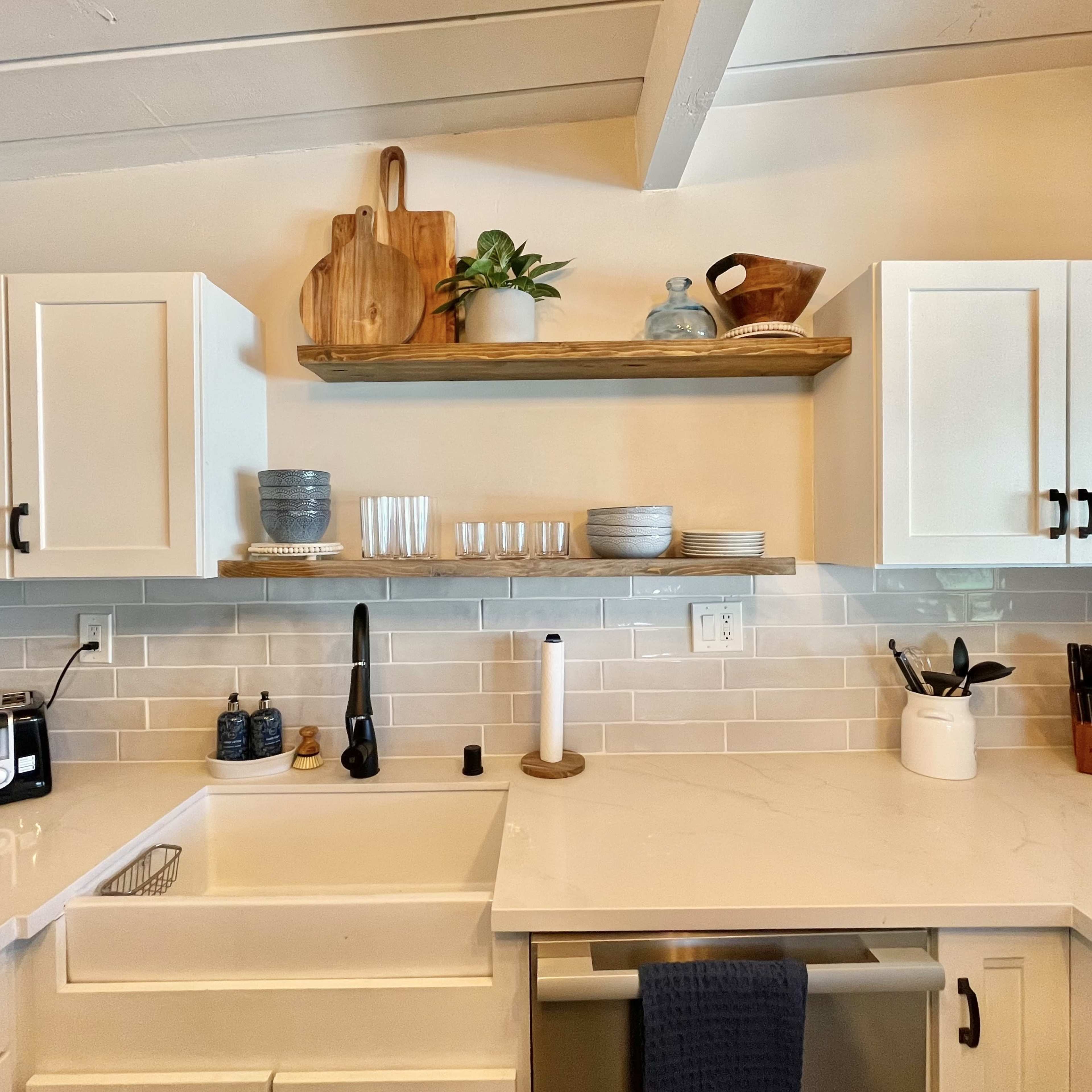 A modern kitchen with white cabinets, a wooden shelf displaying dishes and utensils, and a stainless steel sink.