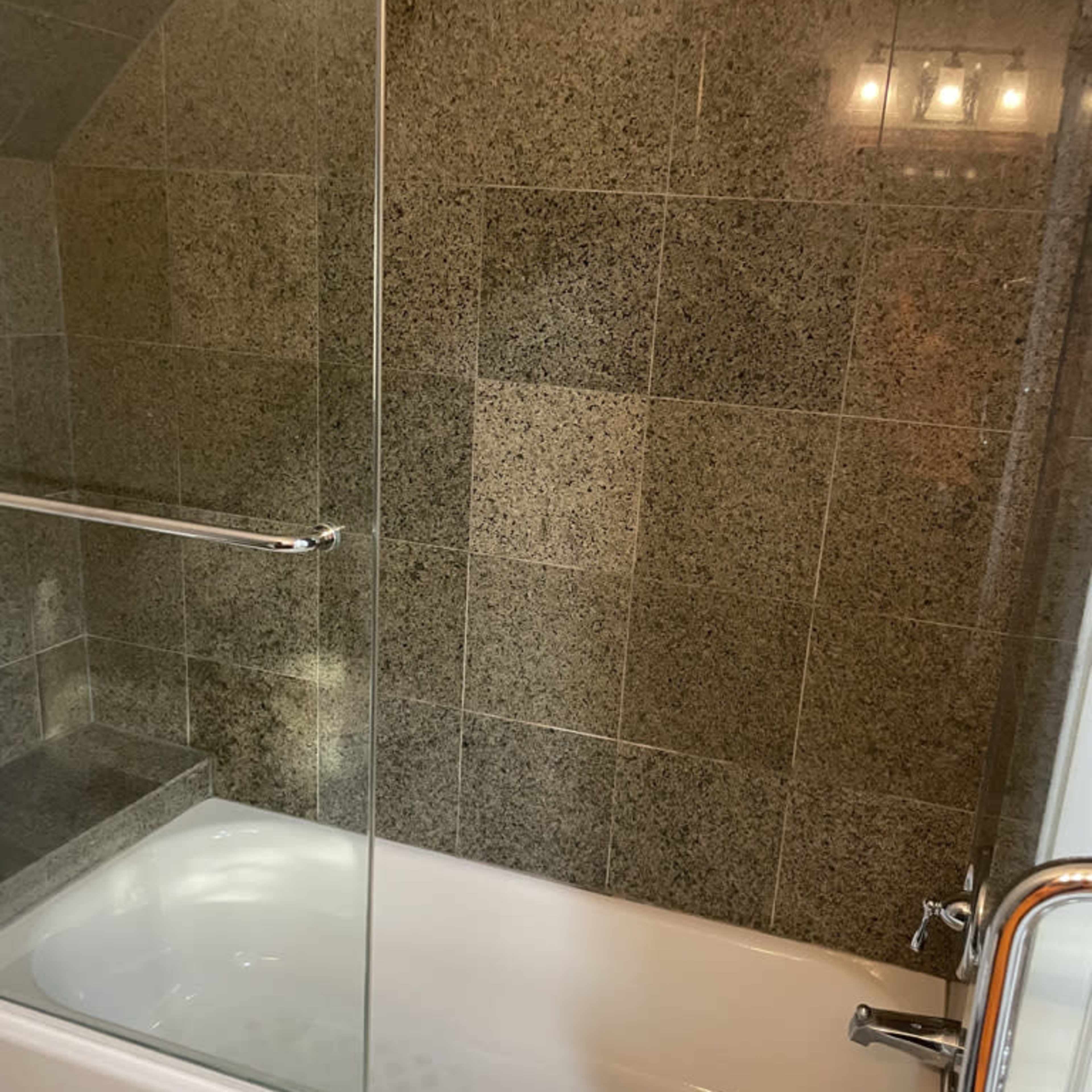 A modern bathroom with a bathtub enclosed by a glass partition and textured, dark stone walls.