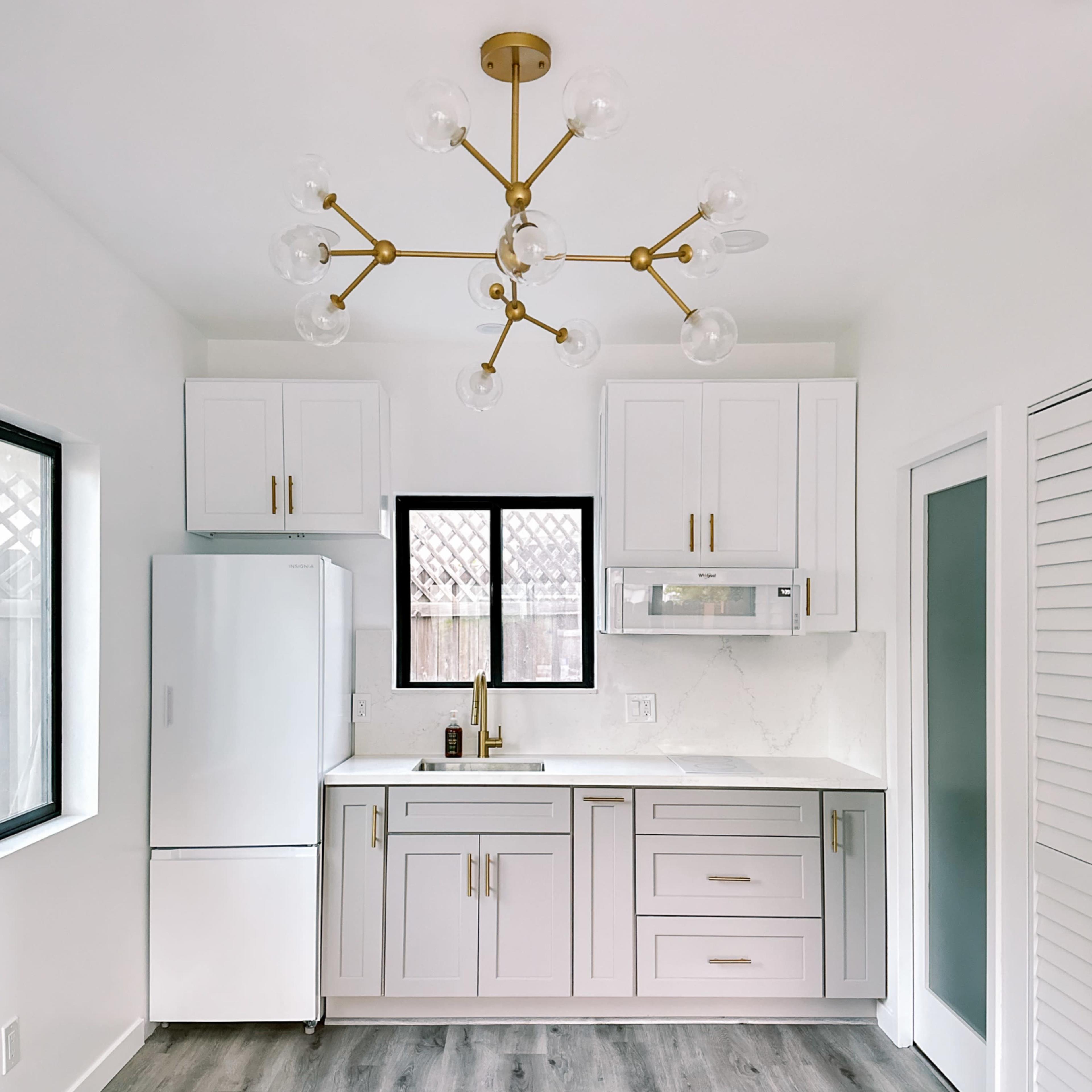 A modern kitchen with white cabinetry, a stainless steel refrigerator, and a brass light fixture.
