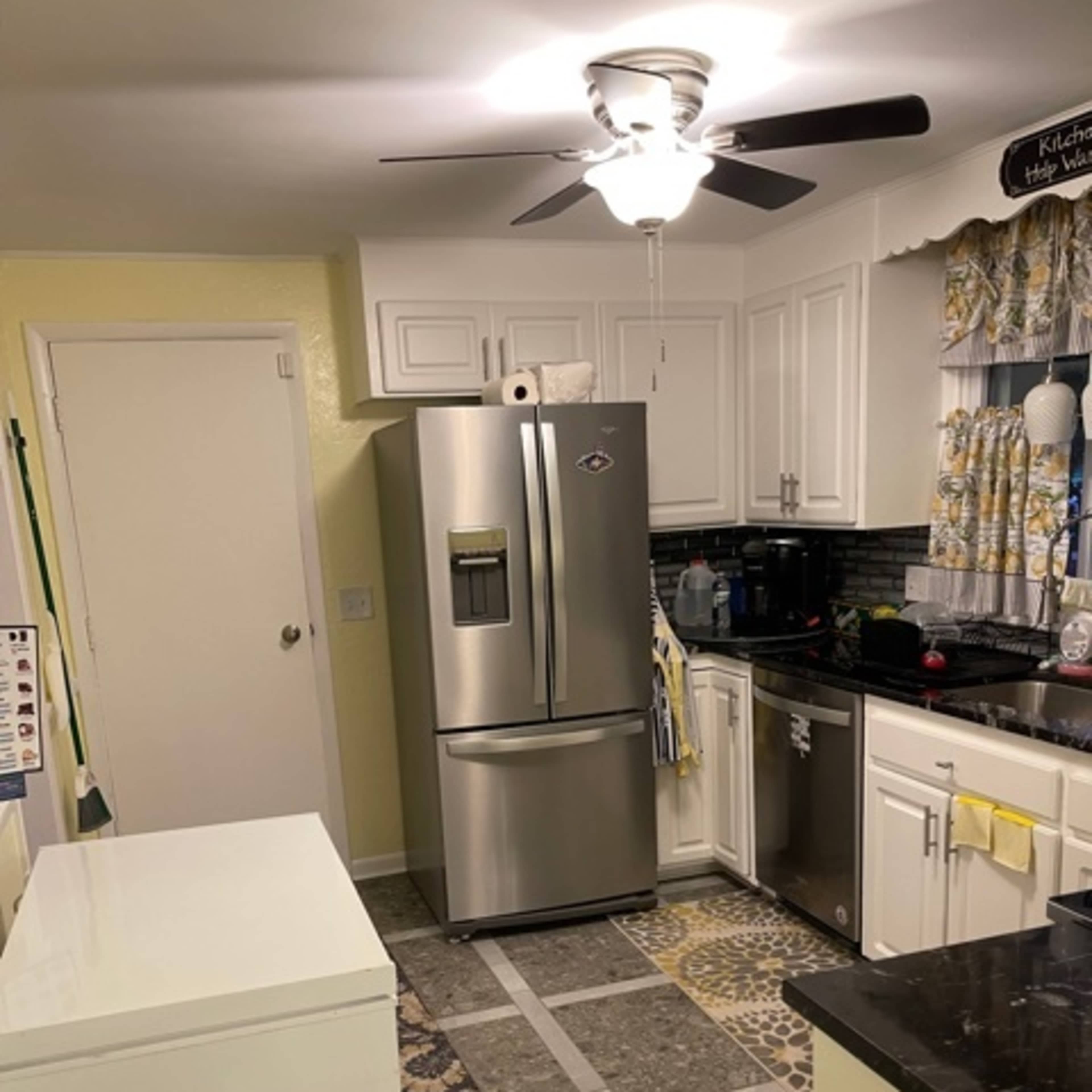 A kitchen featuring a stainless steel refrigerator, white cabinets, a black countertop, and a patterned floor rug.