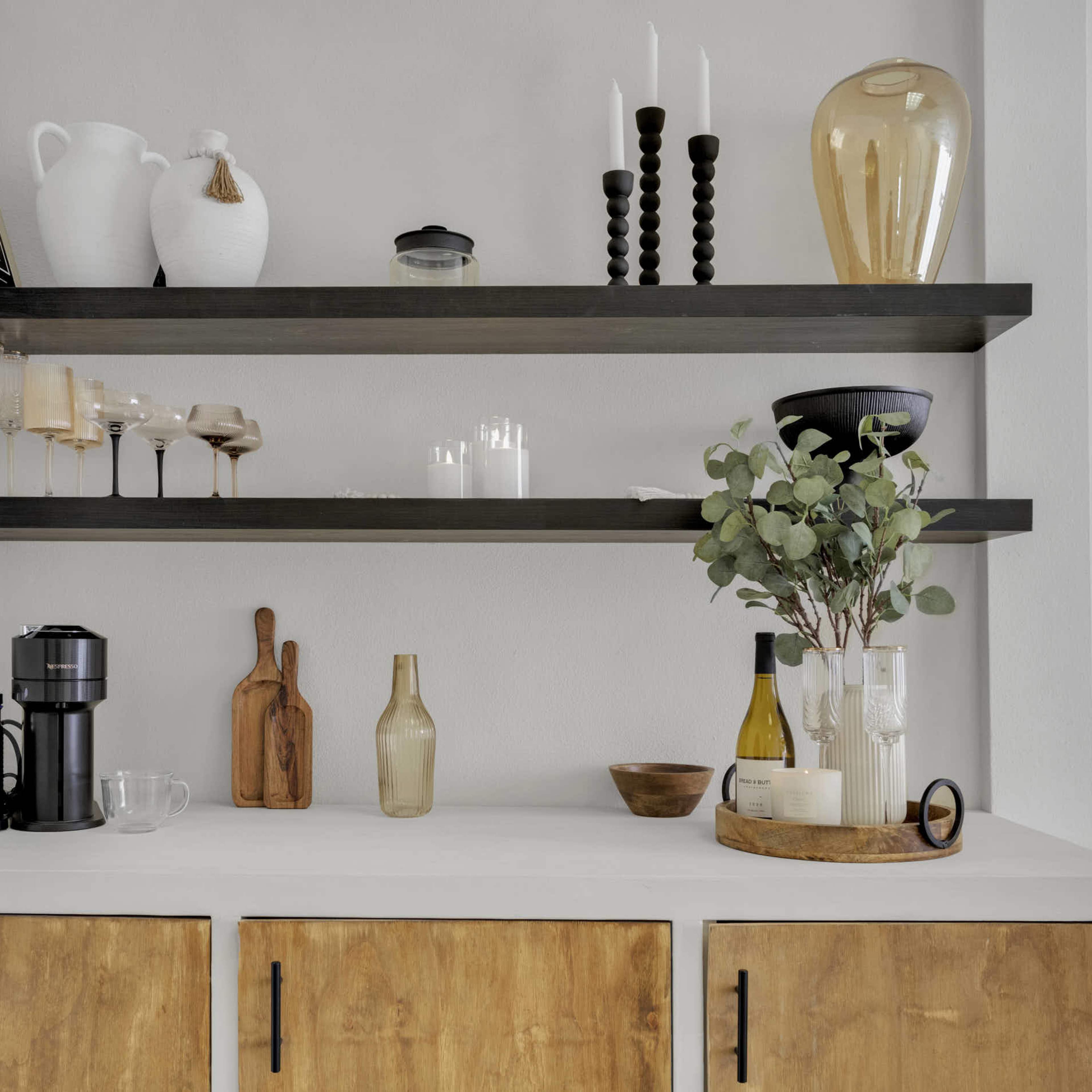 A minimalist shelving unit above a countertop, featuring decorative items, glassware, and kitchen utensils.