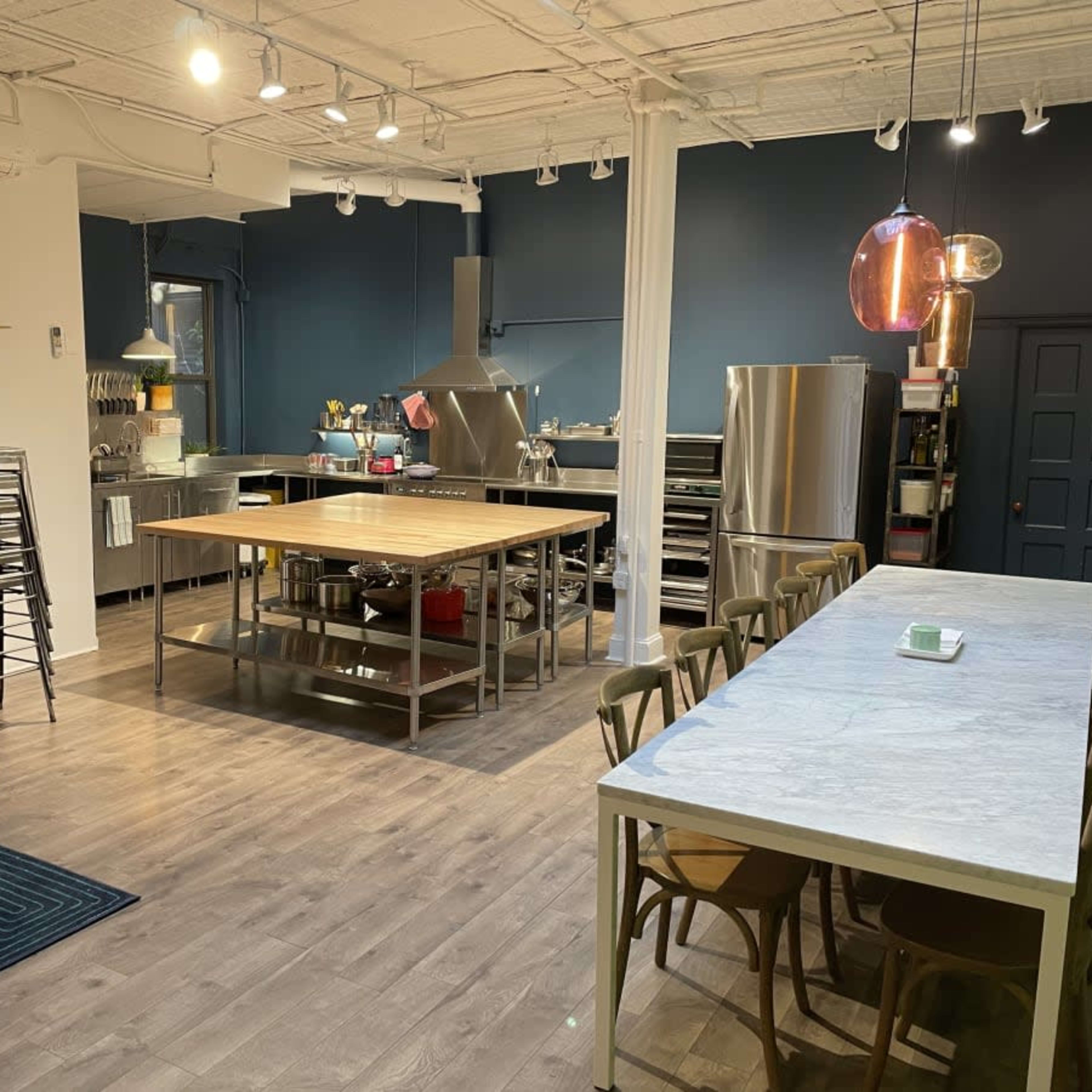 A modern kitchen space featuring a large central table, stainless steel appliances, and a cozy seating area with a pink sofa.