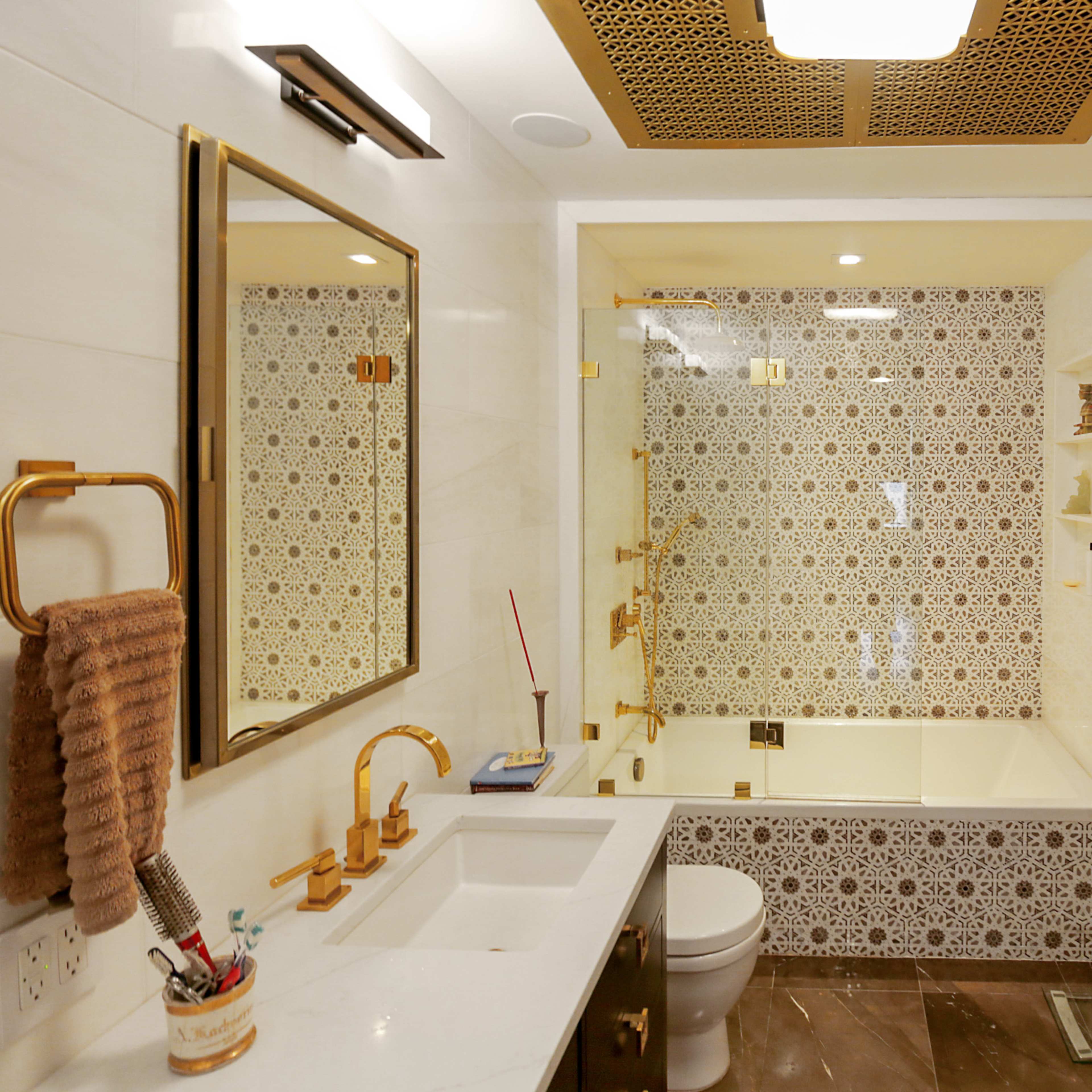 A modern bathroom featuring a gold-accented vanity, a patterned tile shower, and a large mirror.