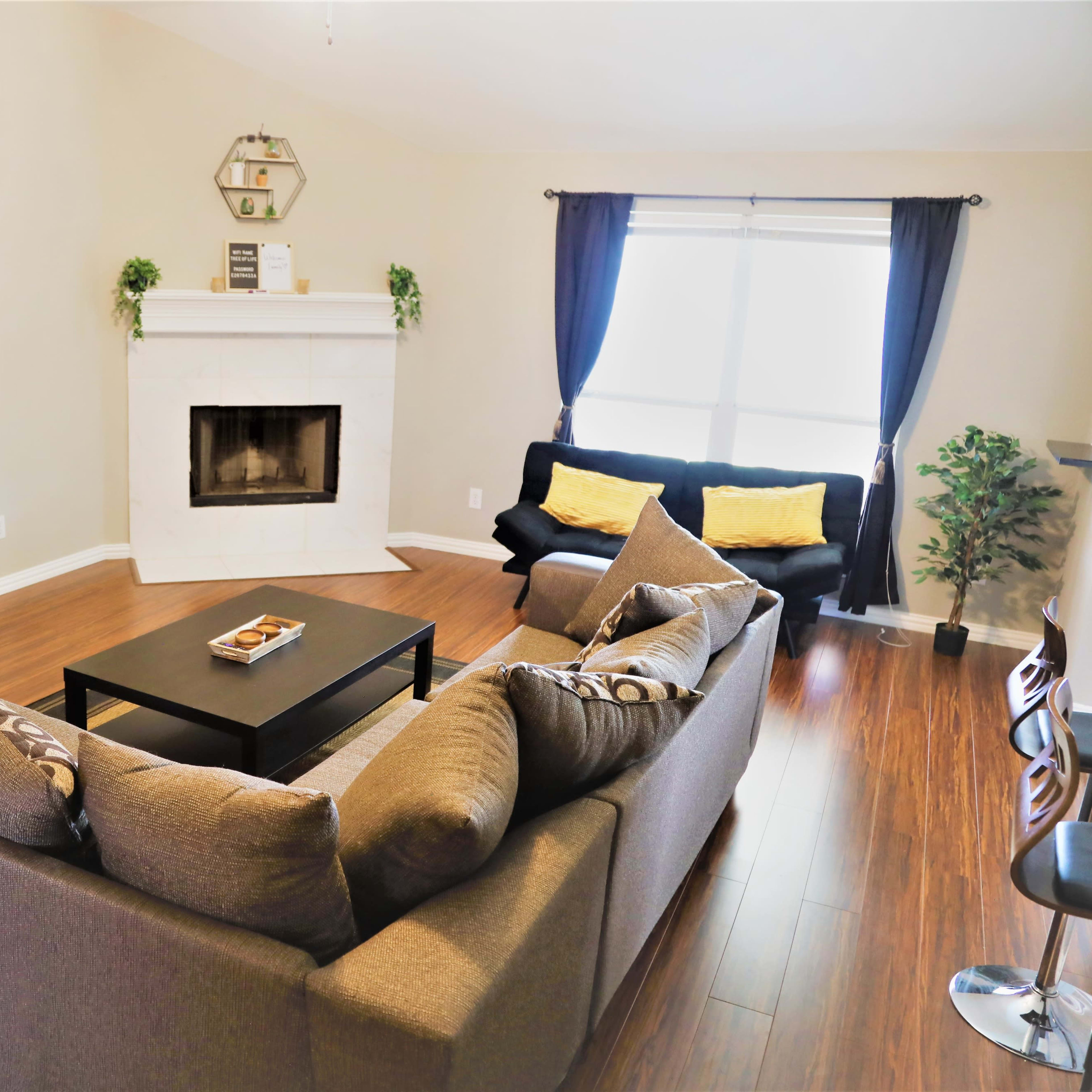 The living room features a gray sectional sofa, a black coffee table, a television mounted on the wall, and a fireplace surrounded by light-colored walls and wooden flooring.