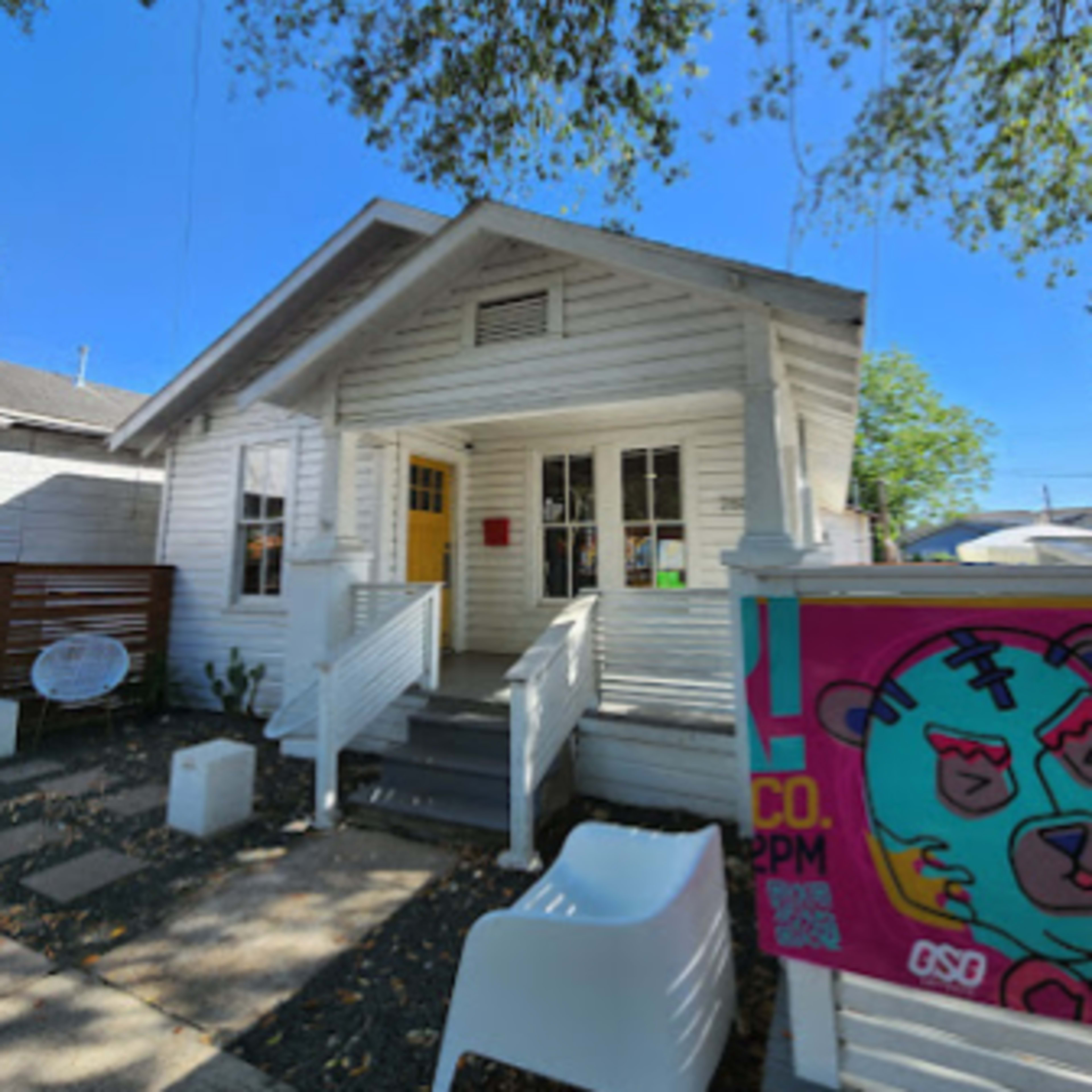 A white wooden house with a front porch and a colorful sign on the right.