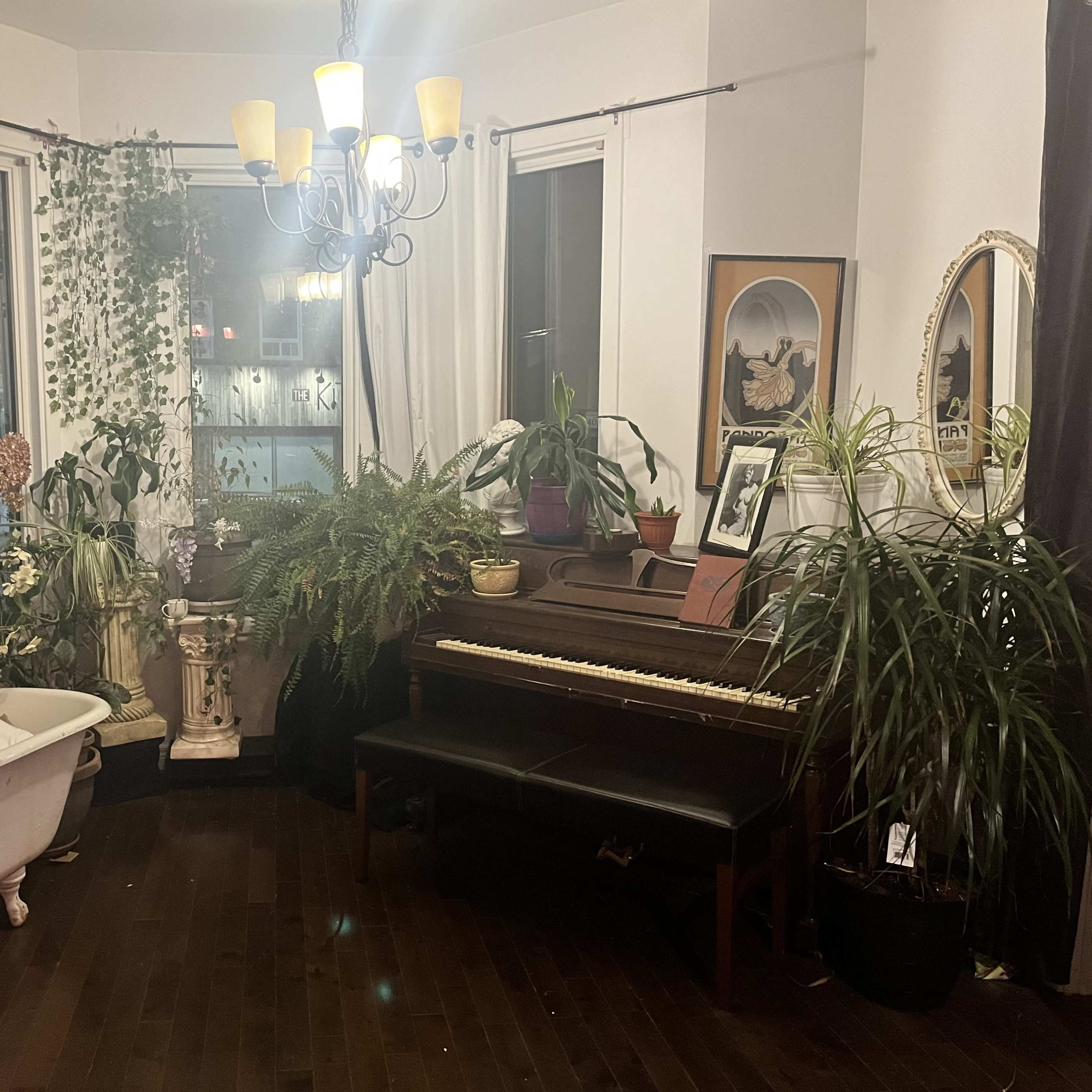 The room features a vintage clawfoot bathtub and a piano surrounded by various plants and decorative elements.