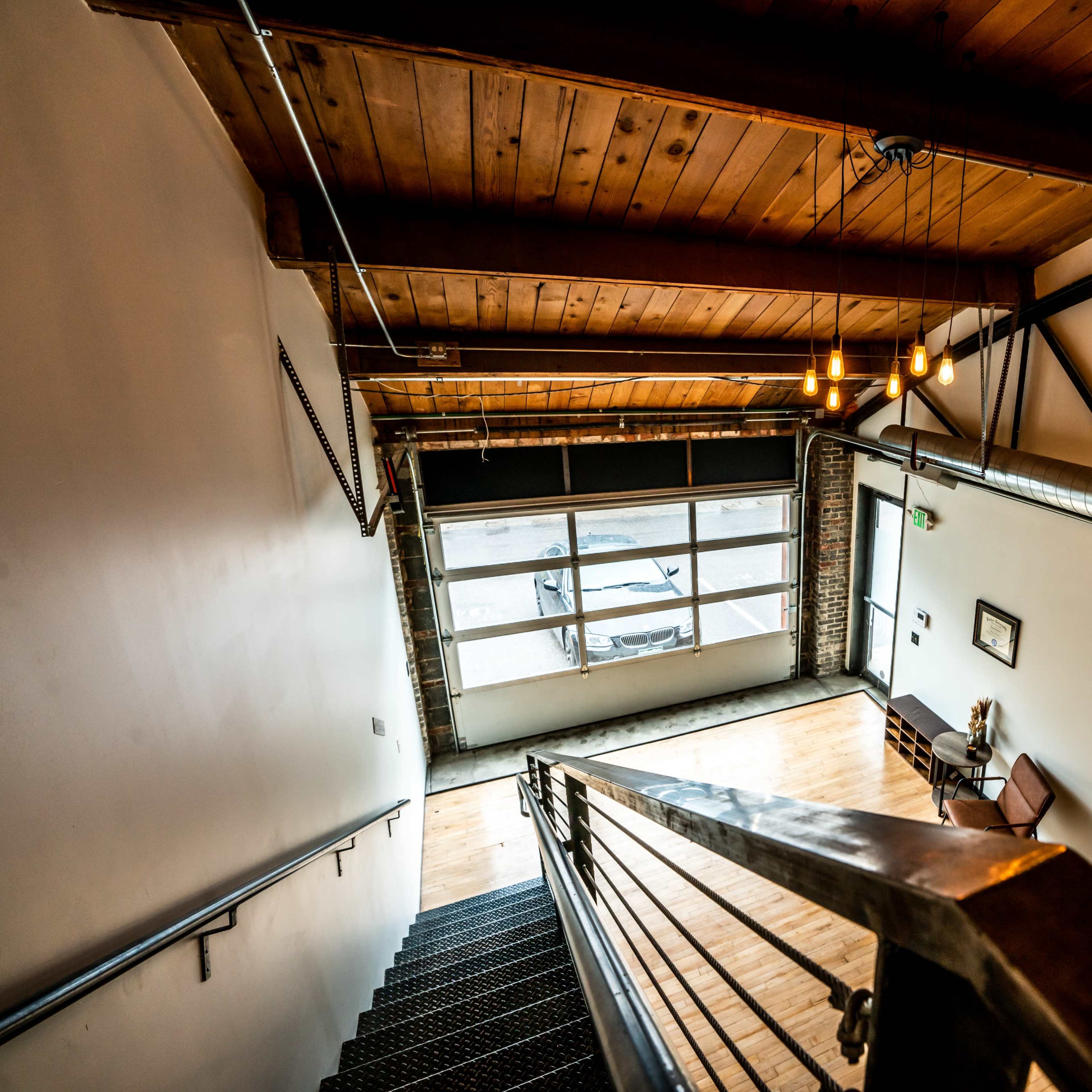 A stairway leading down to a space with large windows, wooden beams, and an industrial-style design.