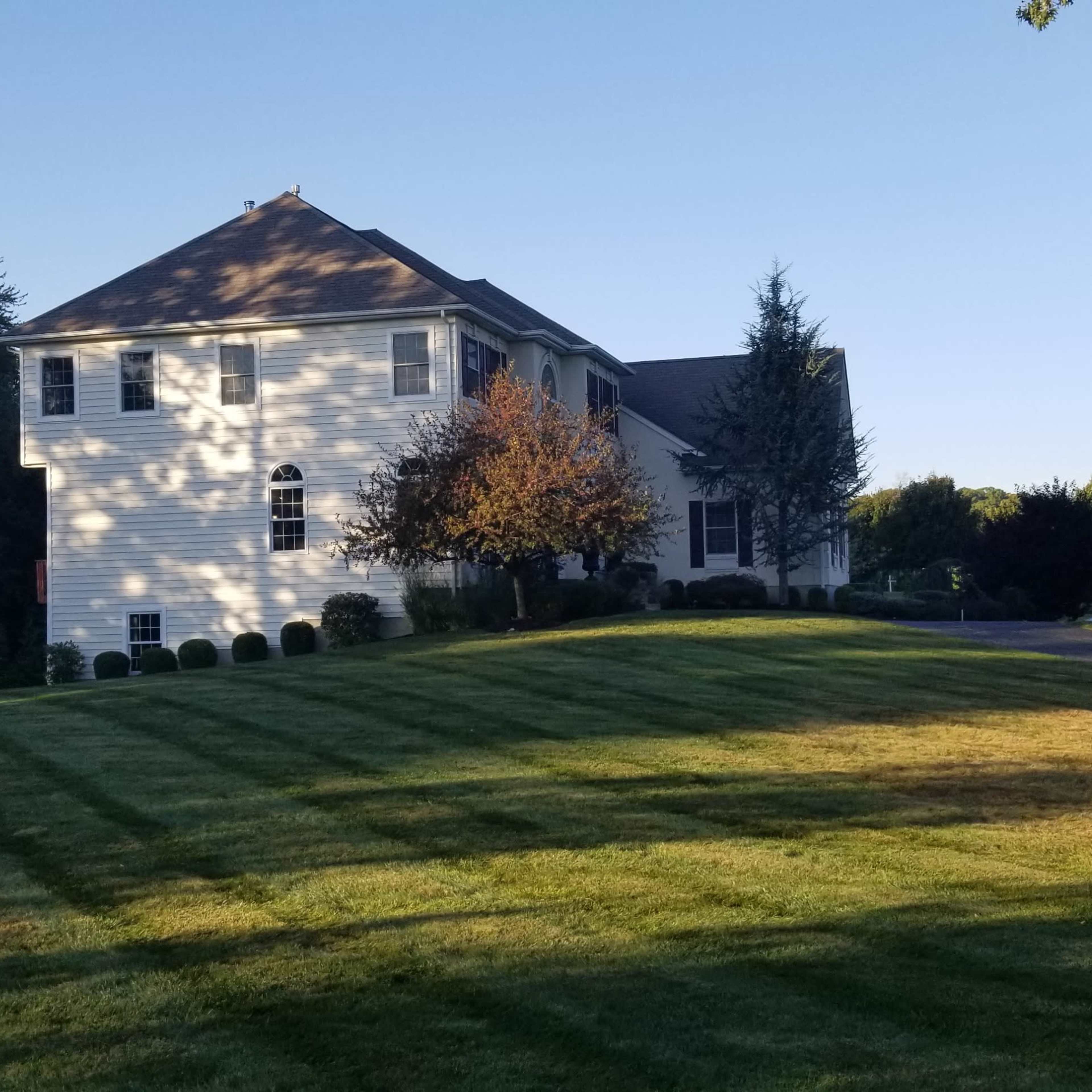 A two-story house with a landscaped lawn and patches of sunlight shines in a clear blue sky.