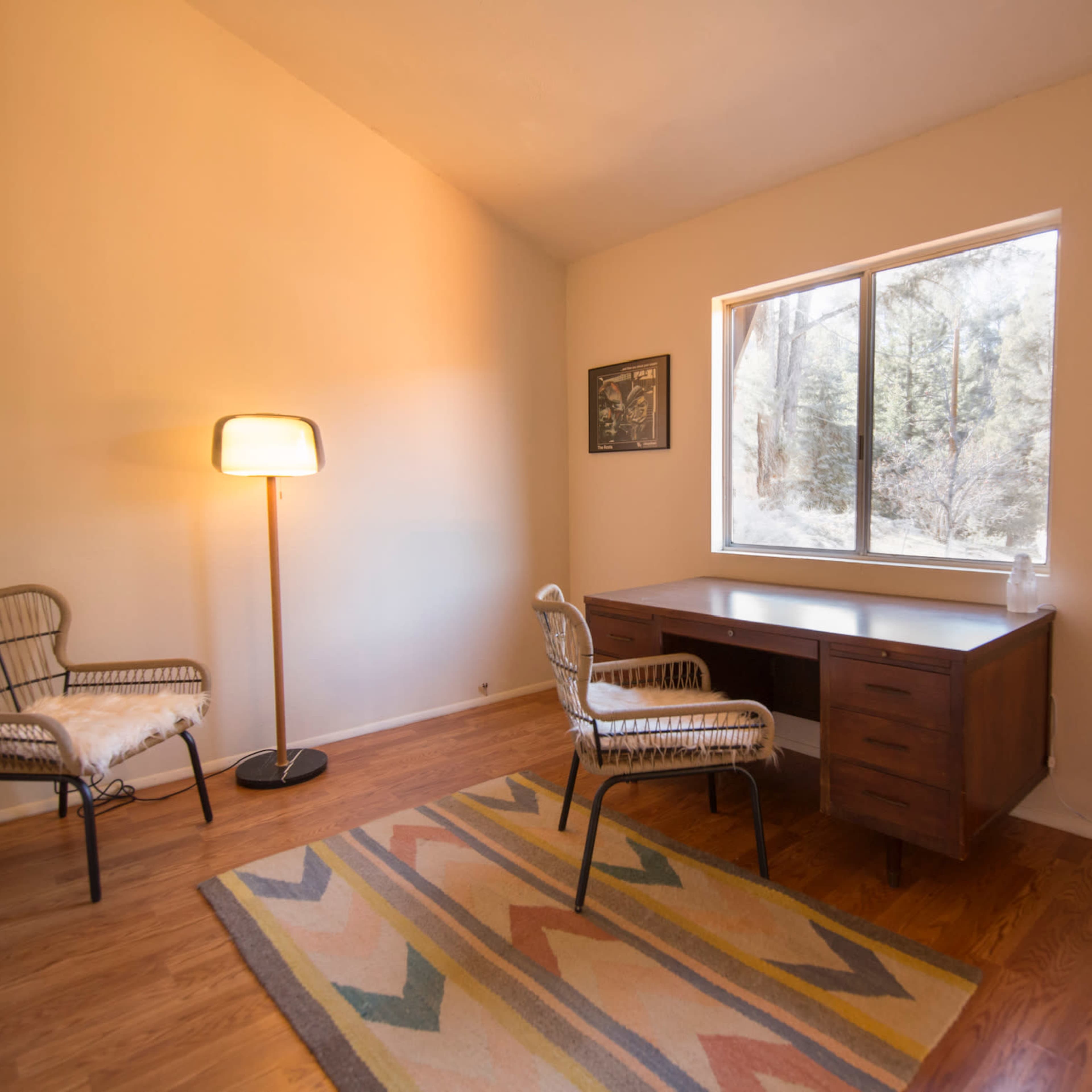 A well-lit room features two chairs and a wooden desk next to a large window overlooking trees.