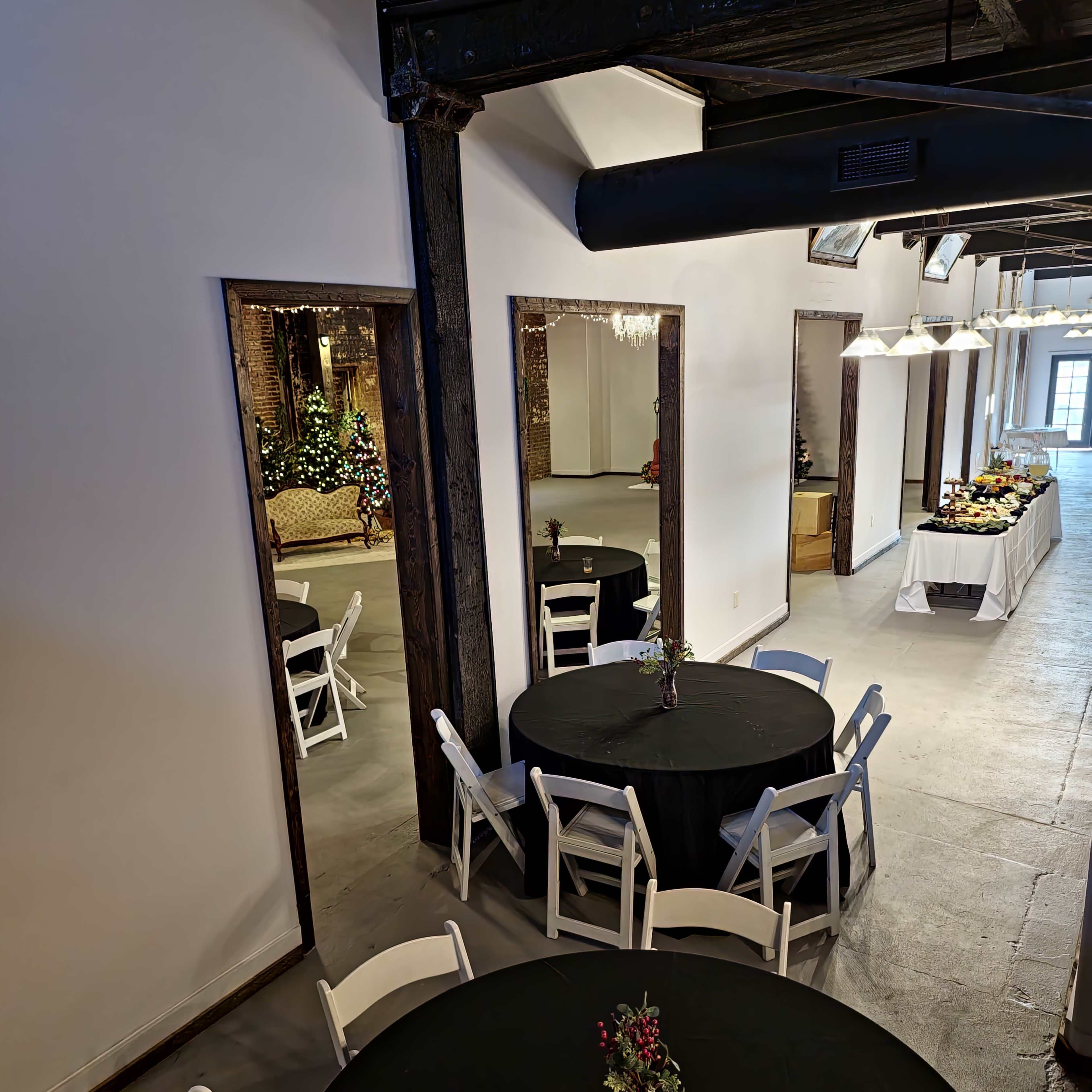 A stylish indoor space with black tables set for dining, mirrors on the walls, and a buffet table in the background.