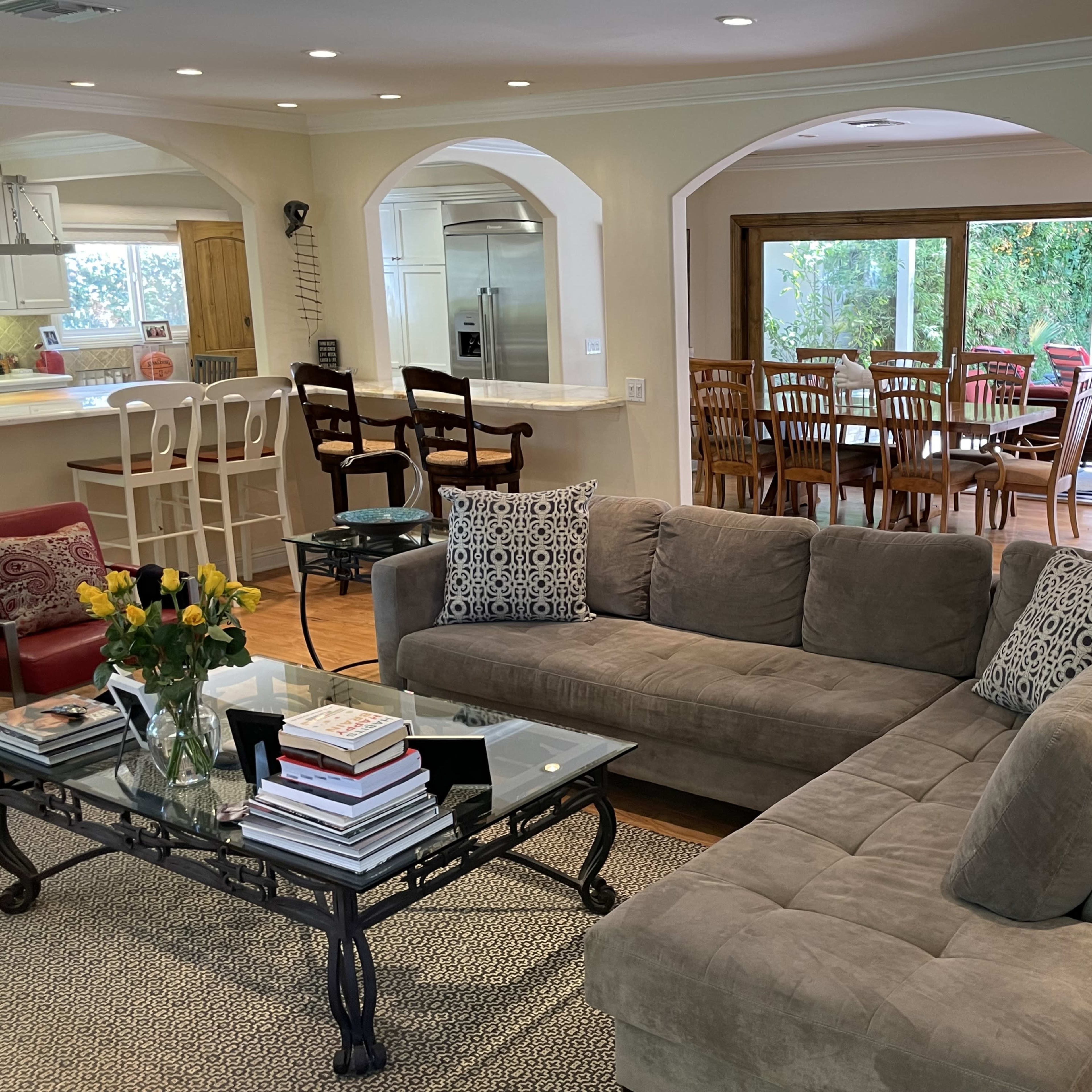 A spacious living room with a sectional sofa, coffee table, and a dining area visible through large windows.