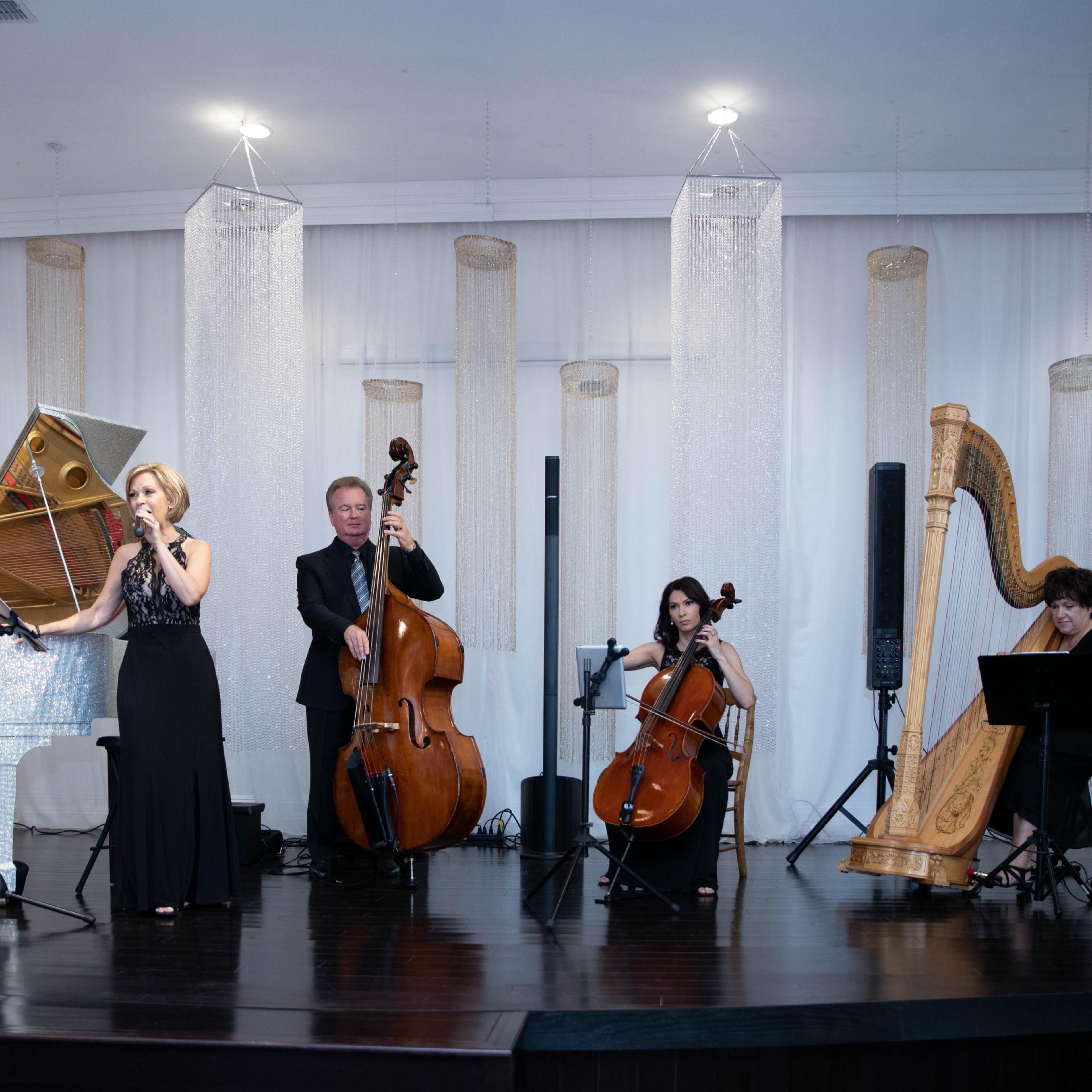 A musical ensemble featuring a pianist, a vocalist, a double bassist, a cellist, and a harpist performs on a stage adorned with decorative lighting.