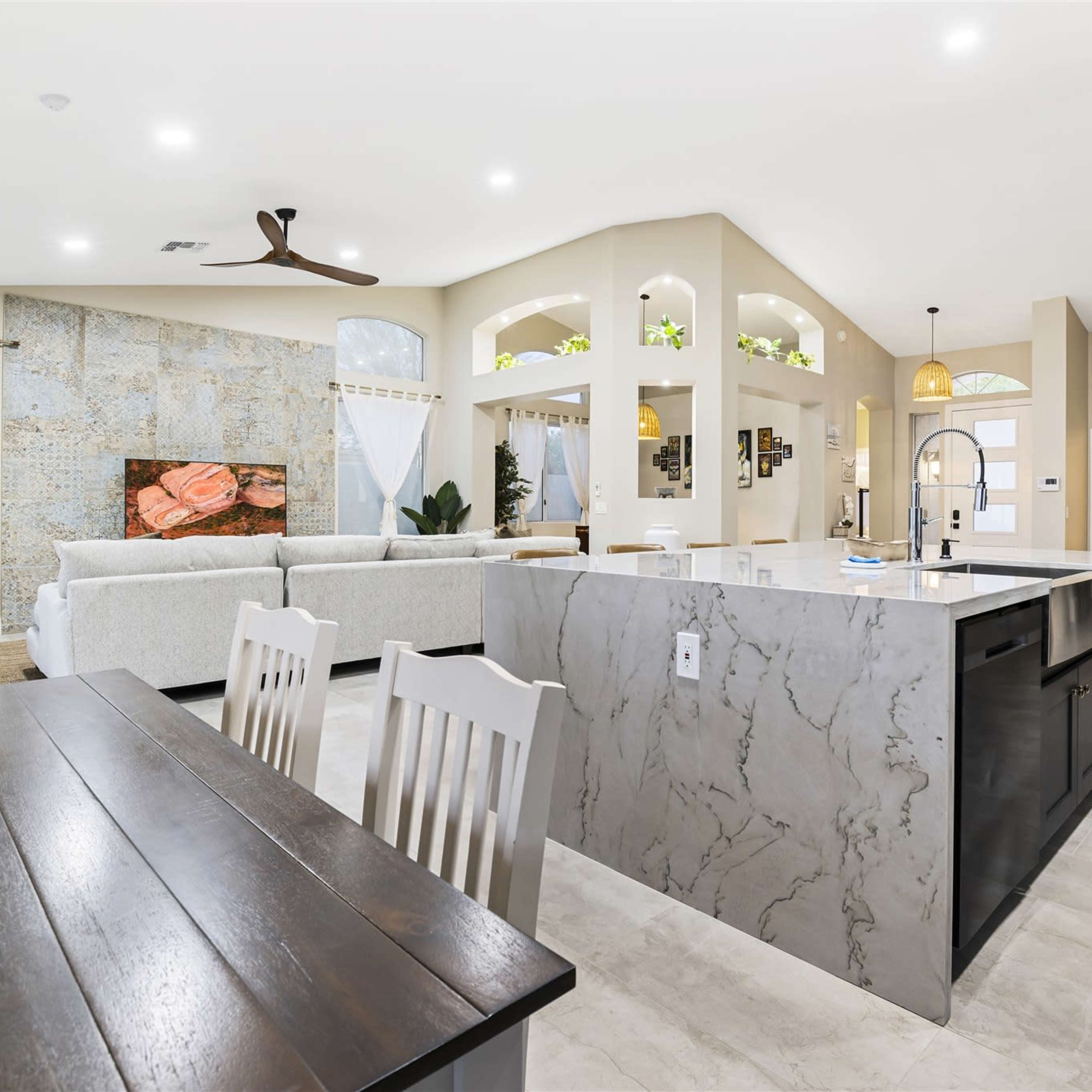 A modern open-concept living space featuring a kitchen island, a dining area, and a cozy seating area with a large window.