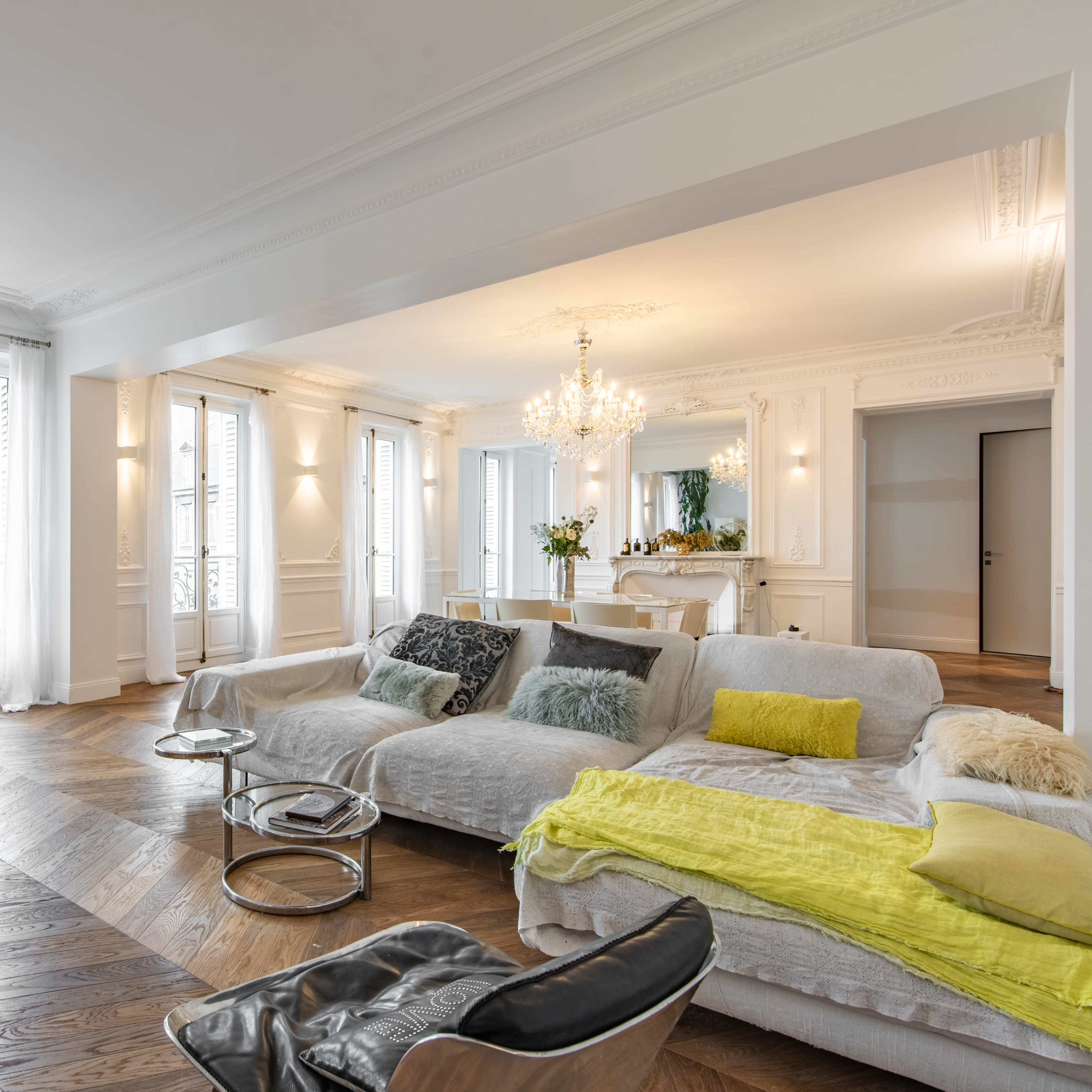 A spacious, elegantly furnished living room with large windows, hardwood floors, and a mix of modern and soft seating arrangements.