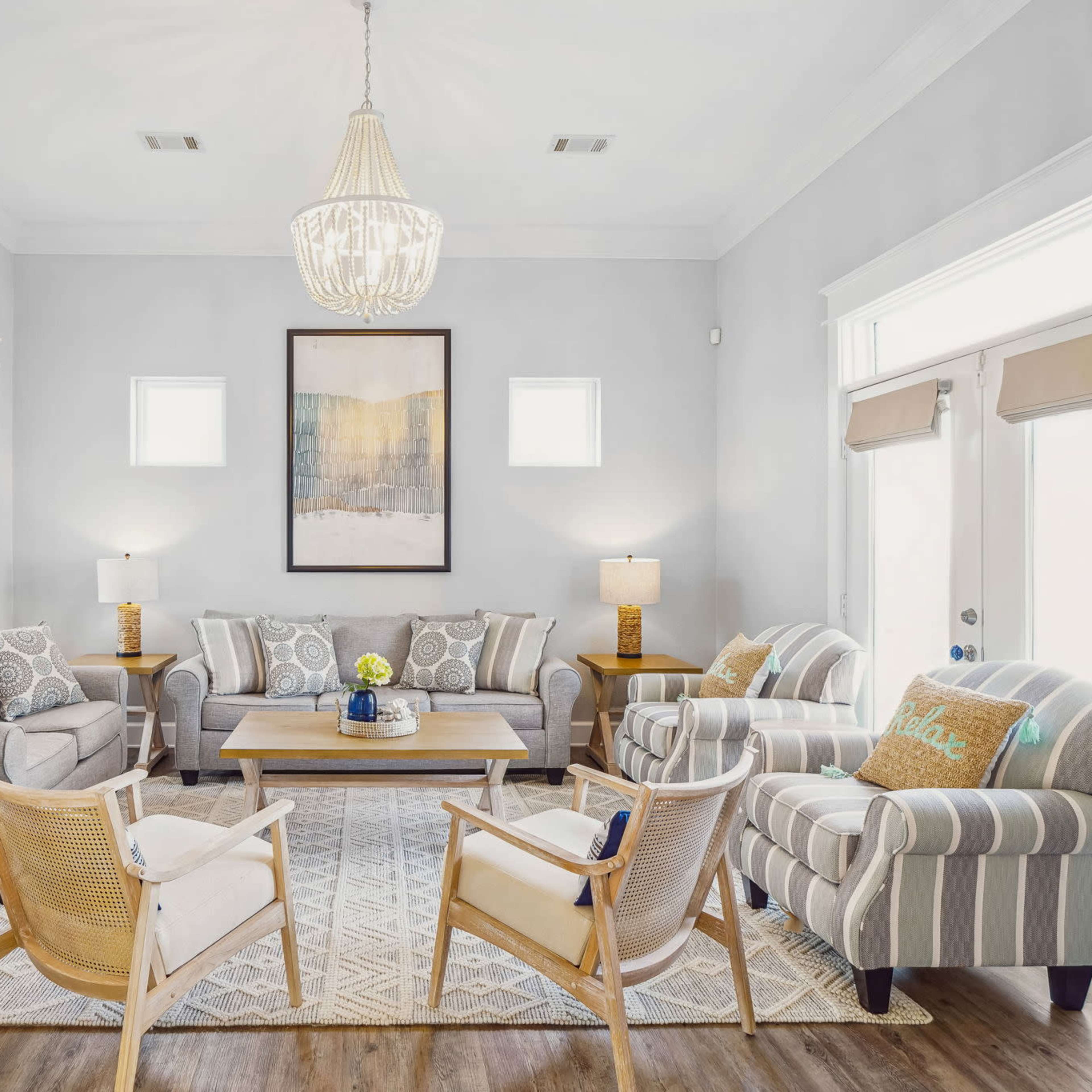 A bright living room features a sofa set, armchairs, a coffee table, and a large rug, with a chandelier hanging from the ceiling.