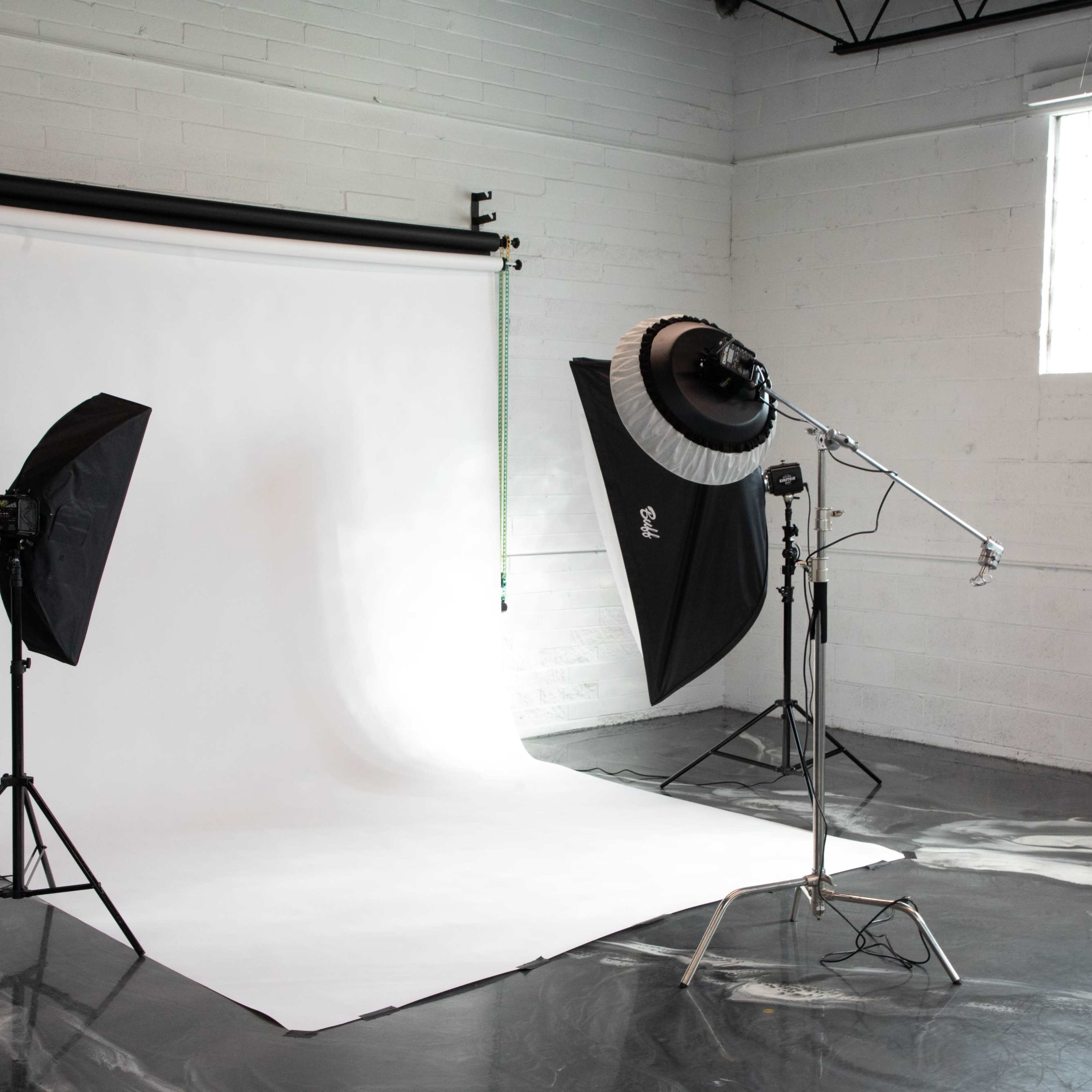 A photography studio setup with a white backdrop, two softbox lights on stands, and a large light modifier.