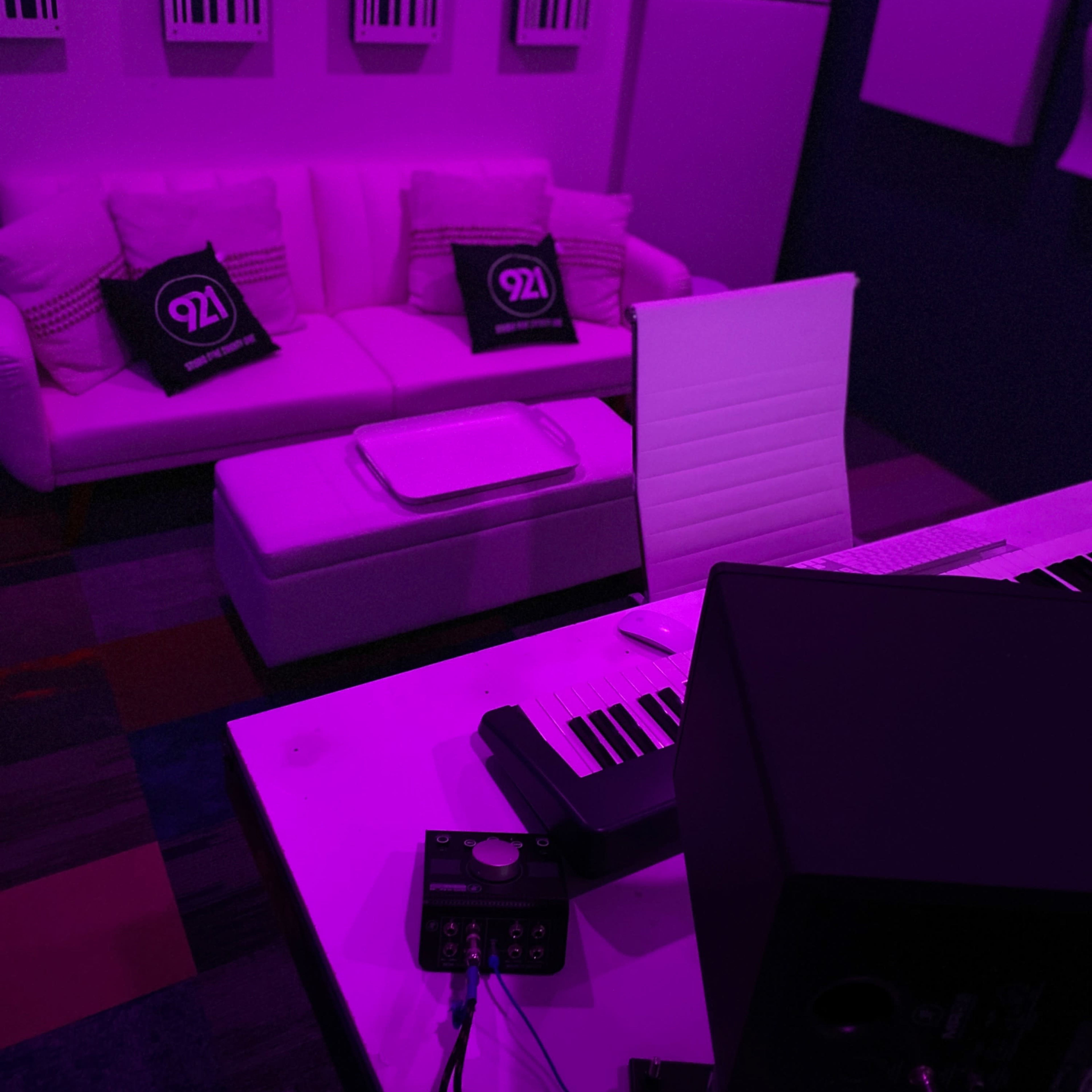 A music studio with a white couch, a coffee table, a keyboard, and purple lighting.