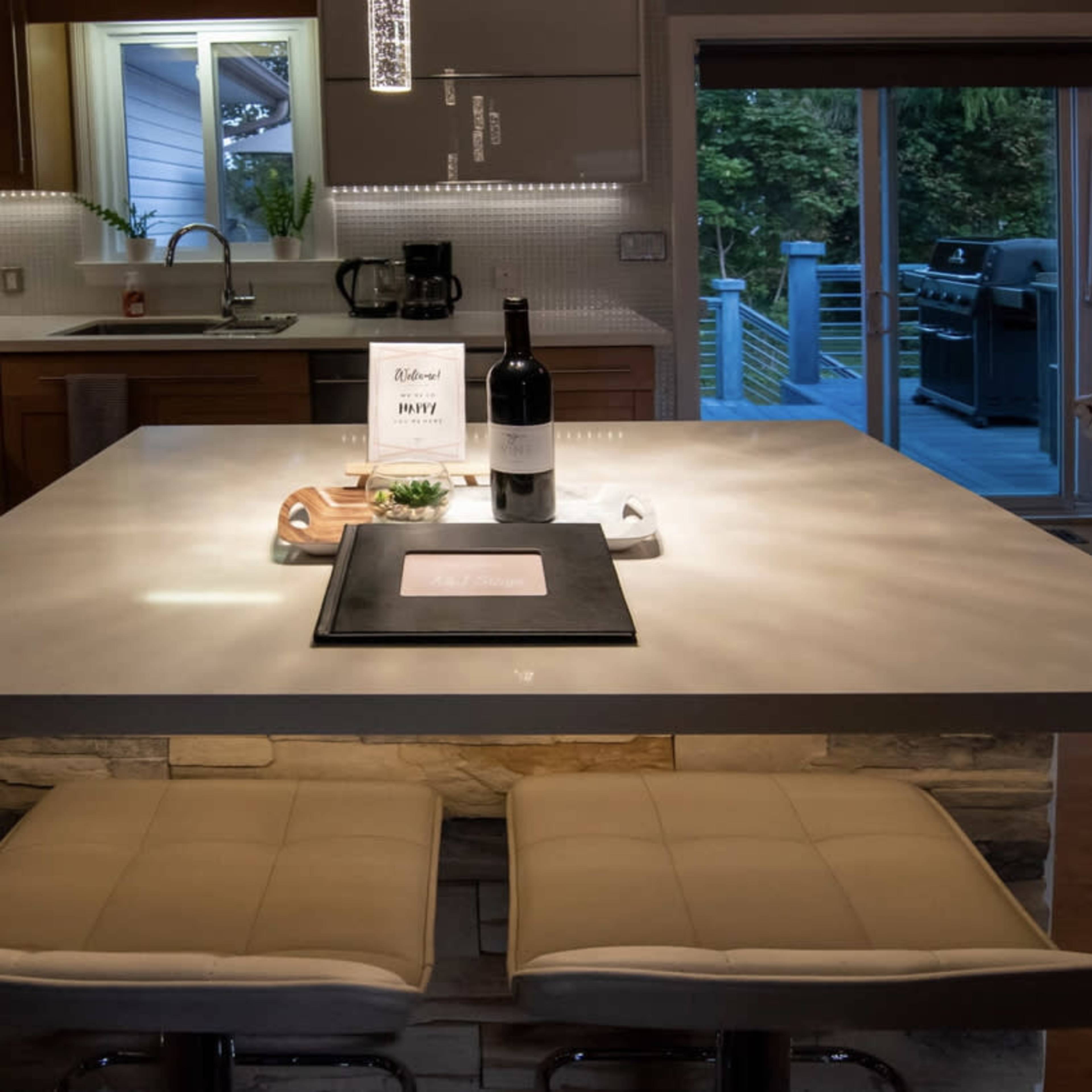The kitchen features a modern island with bar stools, a bottle of wine on the countertop, and warm lighting.