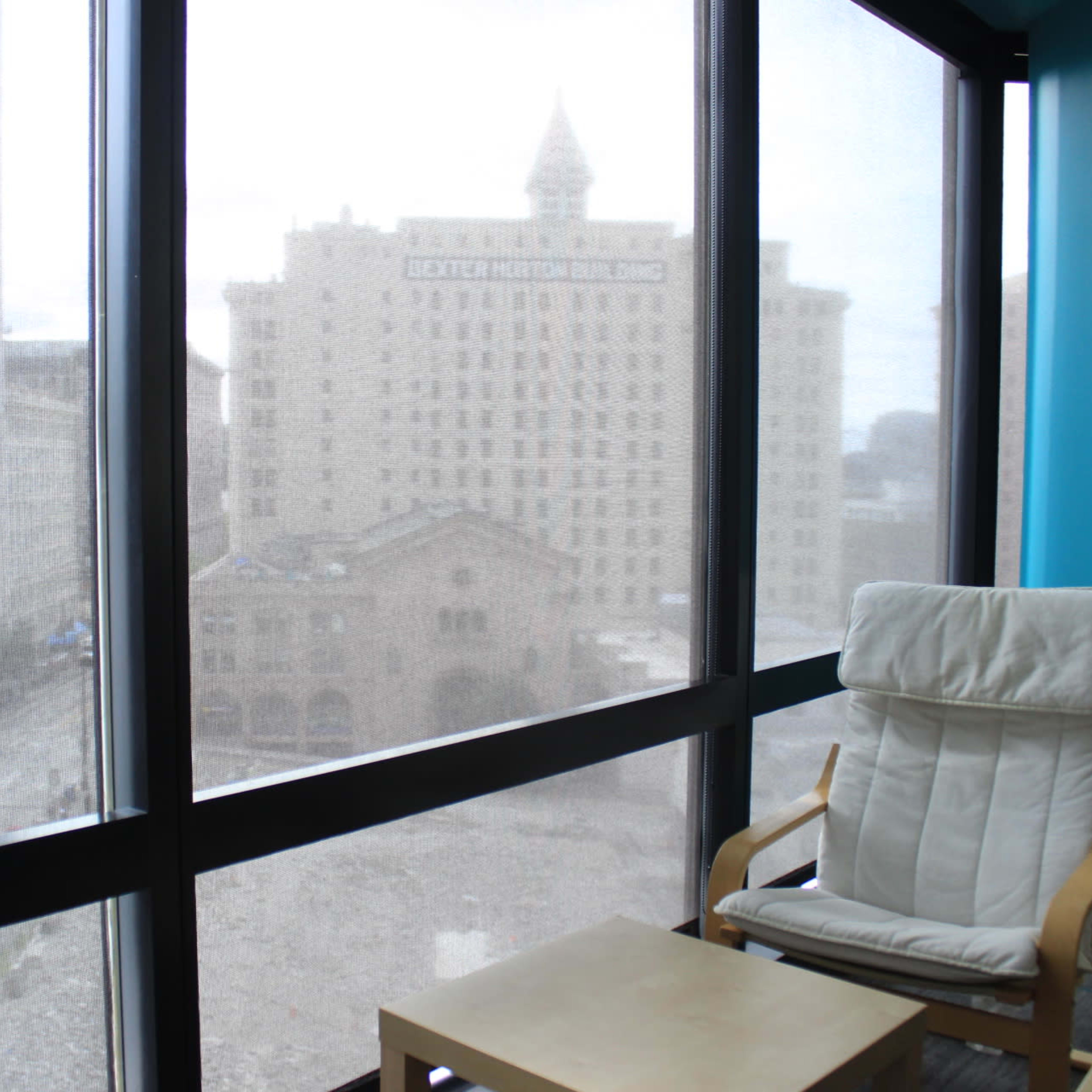 A vacant urban view through large windows, featuring a chair and a small table in the foreground.
