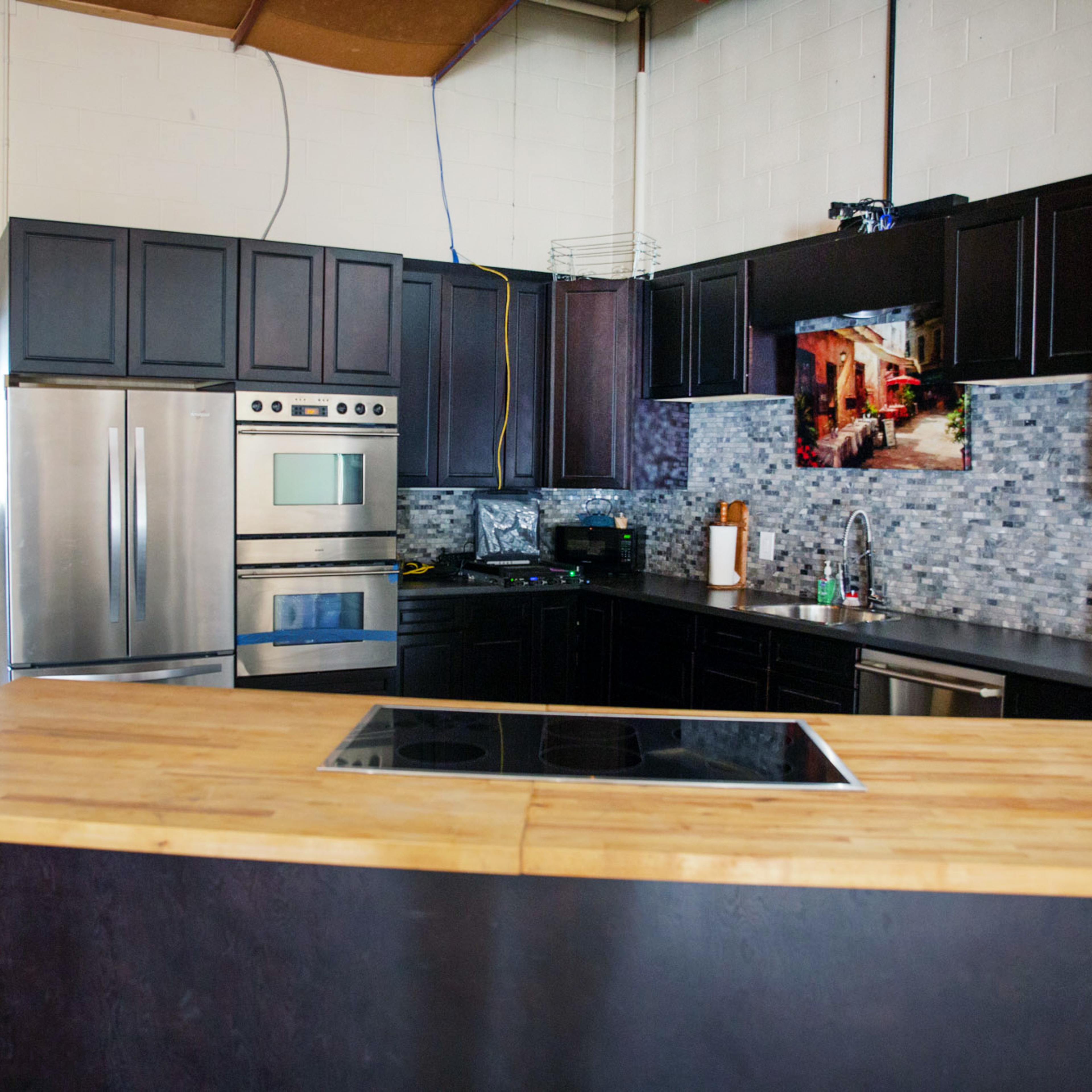 A modern kitchen features dark cabinets, stainless steel appliances, and a large wooden island with a built-in cooktop.