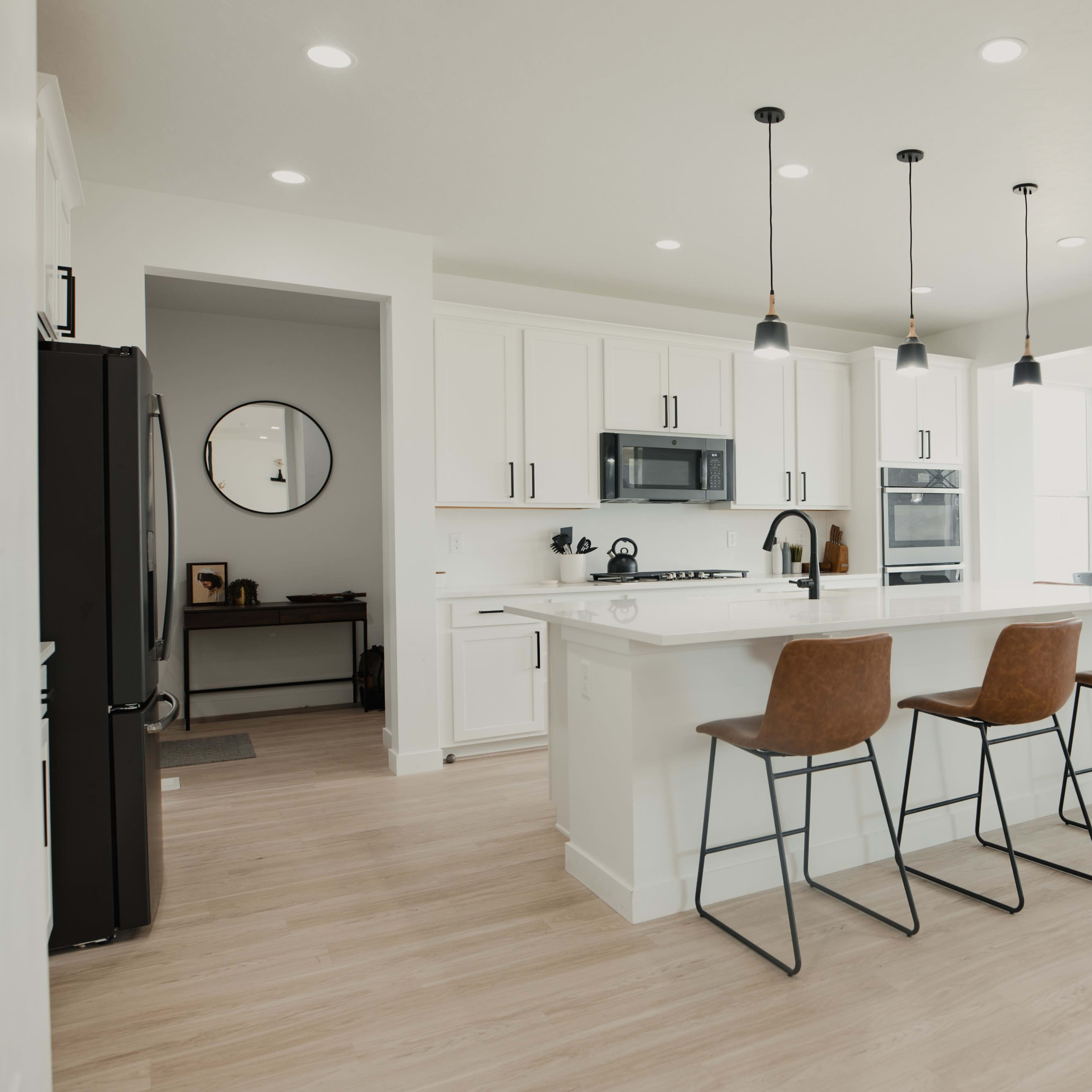 A bright kitchen features a central island with seating, modern appliances, and an open dining area with large windows.